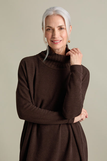 An older woman with gray hair is smiling and wearing a luxurious Allai Rib Neck Soft Jersey Dress against a plain background, making it a versatile addition to your wardrobe.