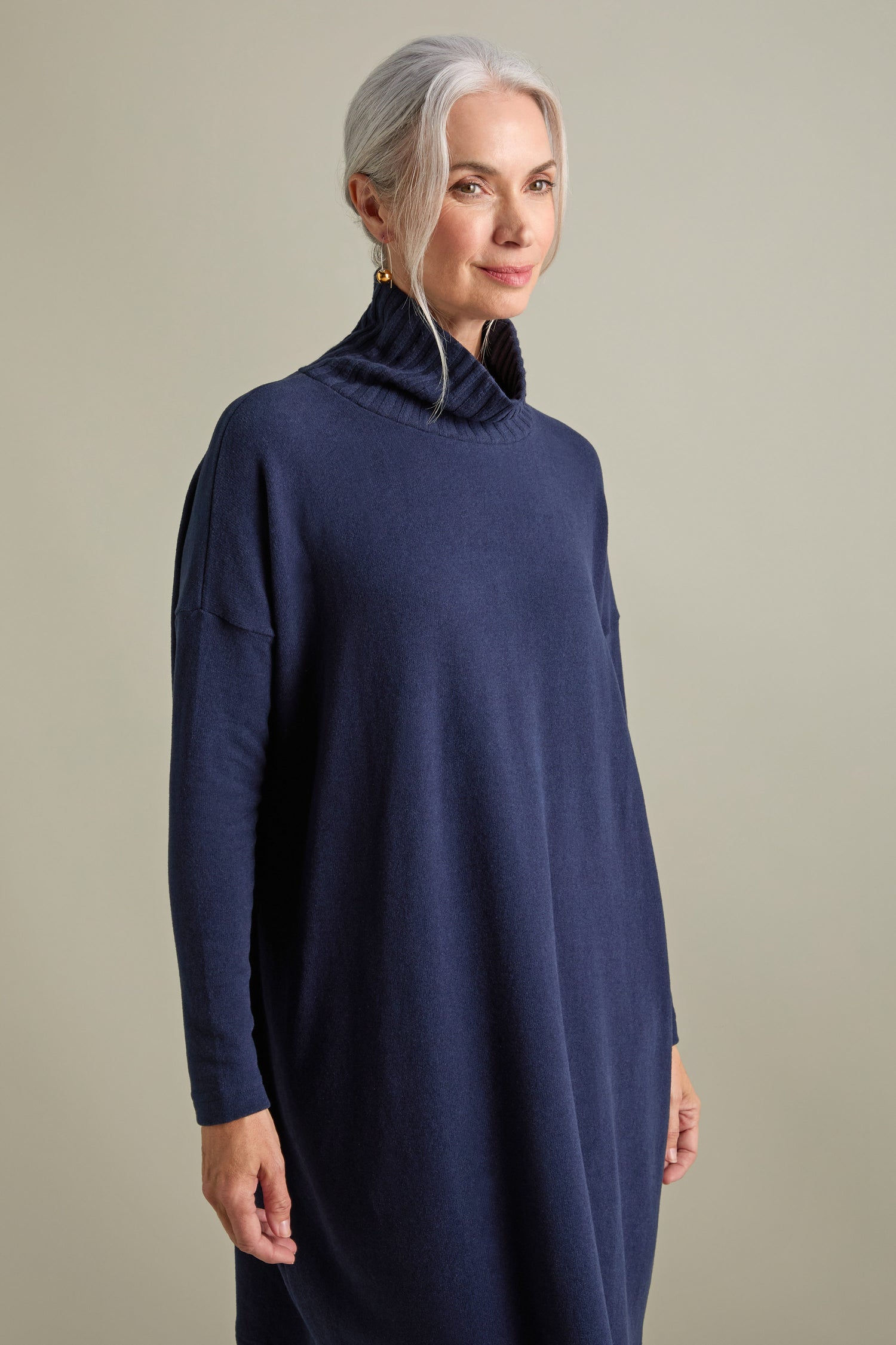 A woman with long gray hair is pictured wearing the Mama B Allai Rib Neck Soft Jersey Dress in navy blue, standing against a plain background. This versatile piece is an effortless blend of comfort and style, making it a perfect addition to any wardrobe.