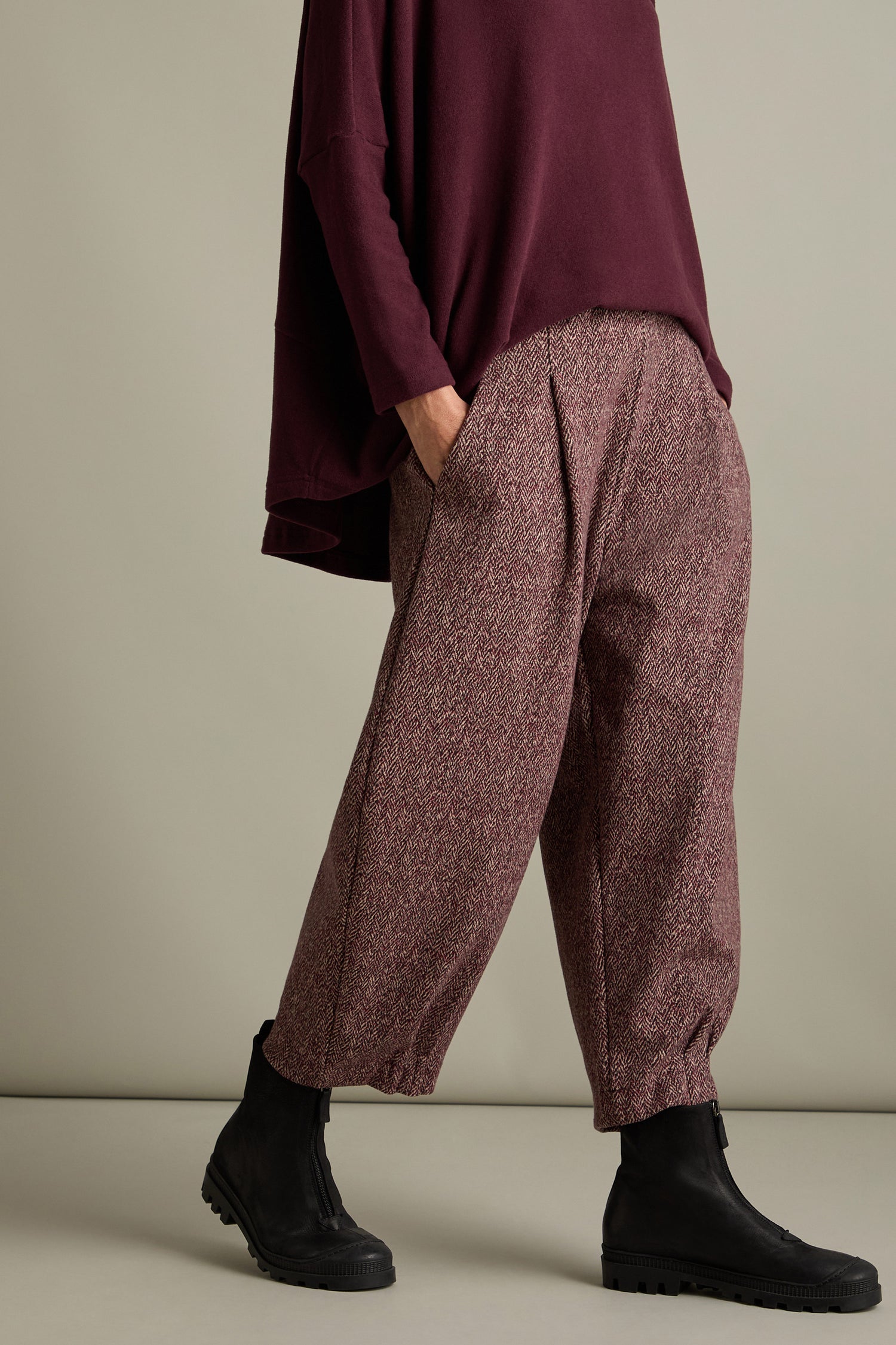 A person wearing a maroon top and Biano Jersey Jacquard Trousers with a chic jacquard print, paired with black ankle boots, poses against a beige background.