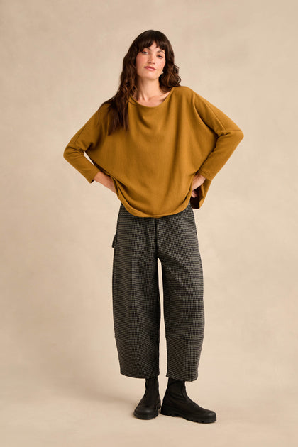 A person standing with hands on hips, wearing Mini Check Jersey Pocket Trousers featuring a cropped leg in soft cotton-blend jersey, paired with a mustard yellow sweater and black boots against a plain beige background.