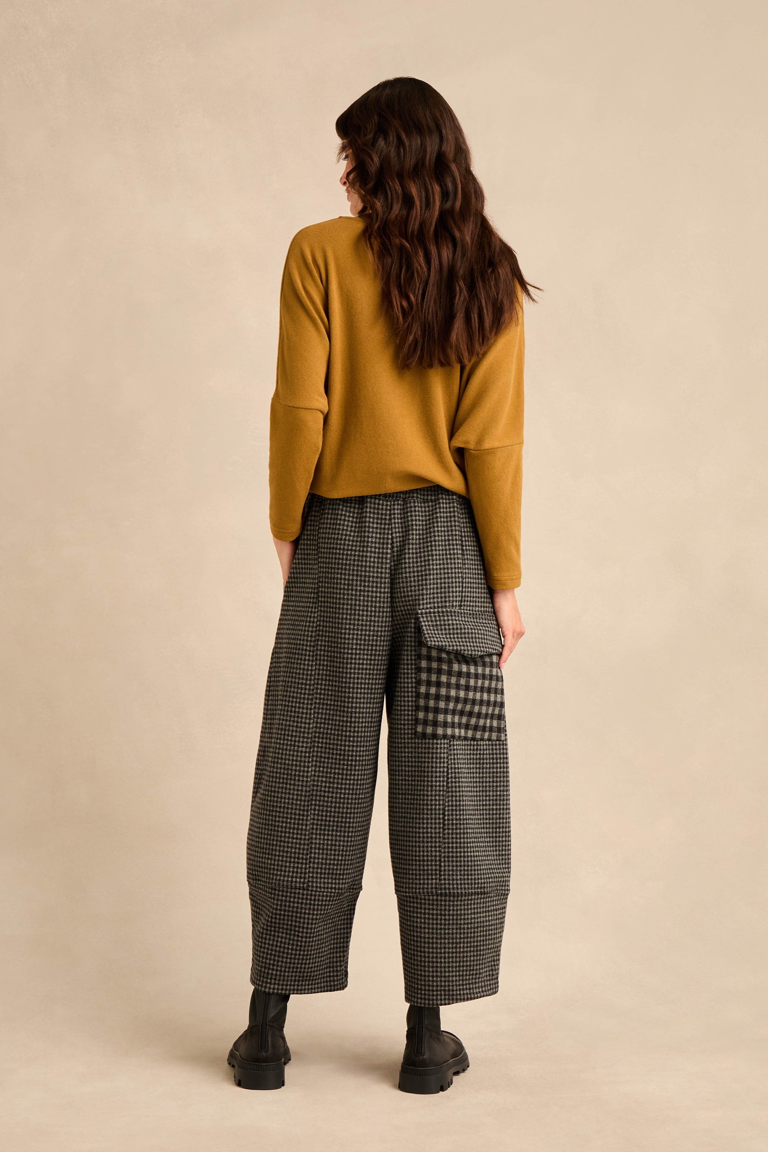 A person stands with their back to the camera, wearing a mustard cotton-blend jersey sweater and the Mini Check Jersey Pocket Trousers—featuring a wide-legged fit, mini check pattern, patch pocket, and cropped leg—paired with black shoes, against a neutral background.