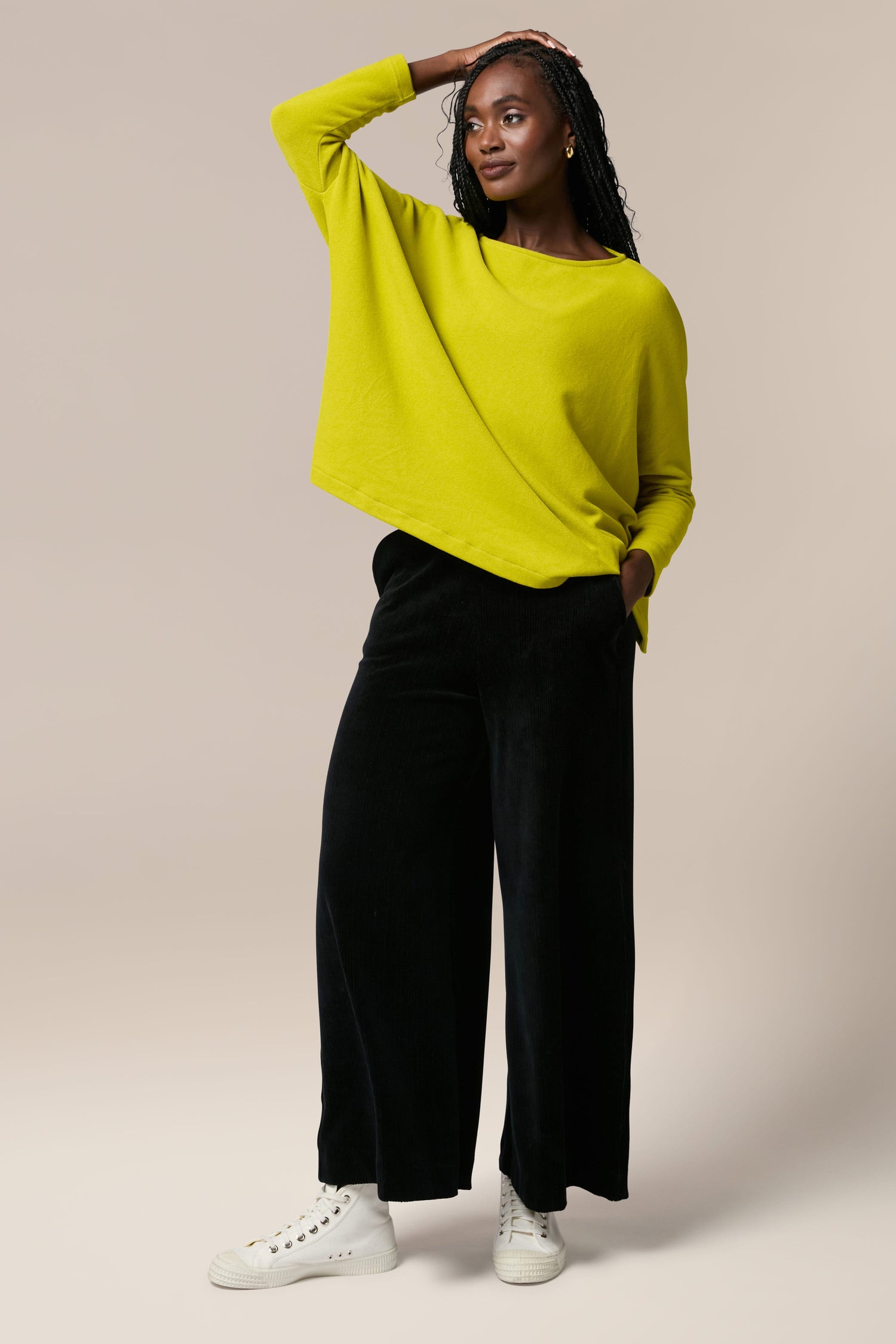 A woman wearing a yellow sweater and black wide leg pants made from cord fabric, highlighting the trendy Bulbo Velvet Wide Leg Trouser style.