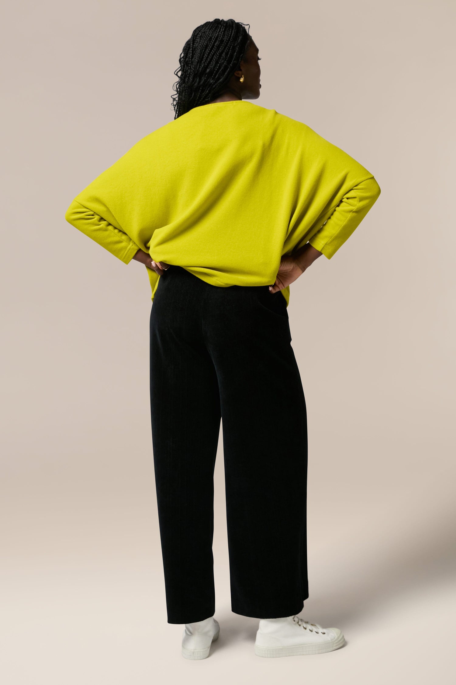 The back view of a woman wearing a yellow sweater and Bulbo Velvet Wide Leg Trouser in cord fabric.