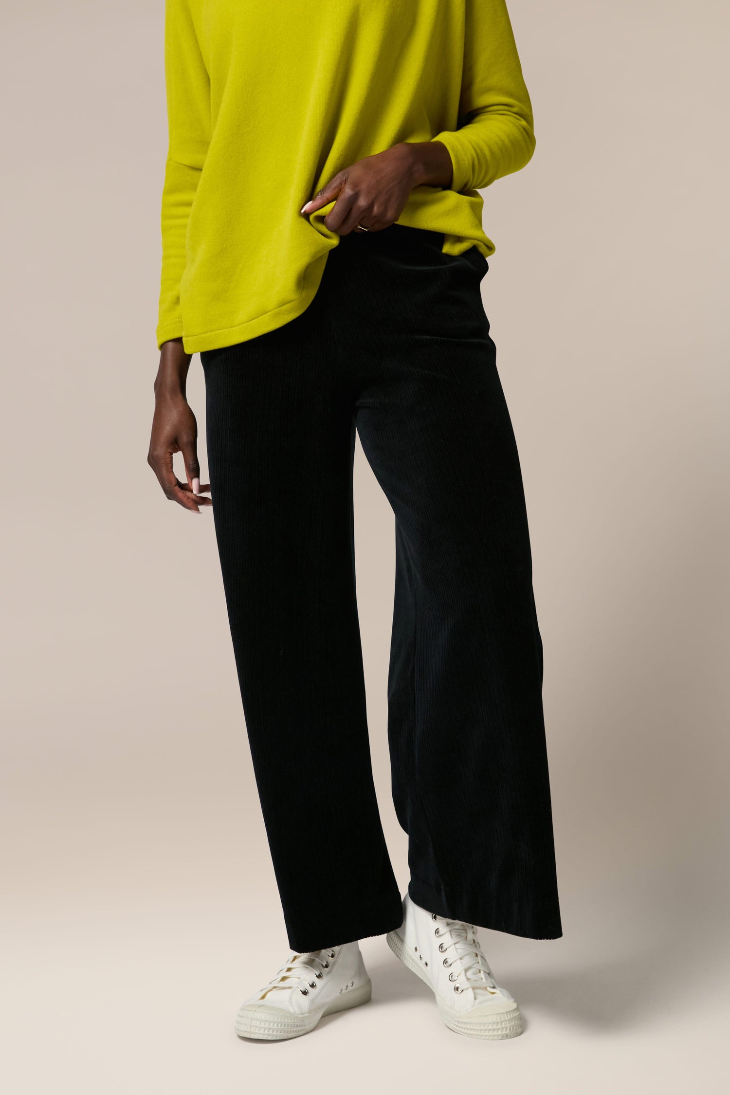 A woman wearing a yellow sweater and Bulbo Velvet Wide Leg Trousers made of cord fabric.