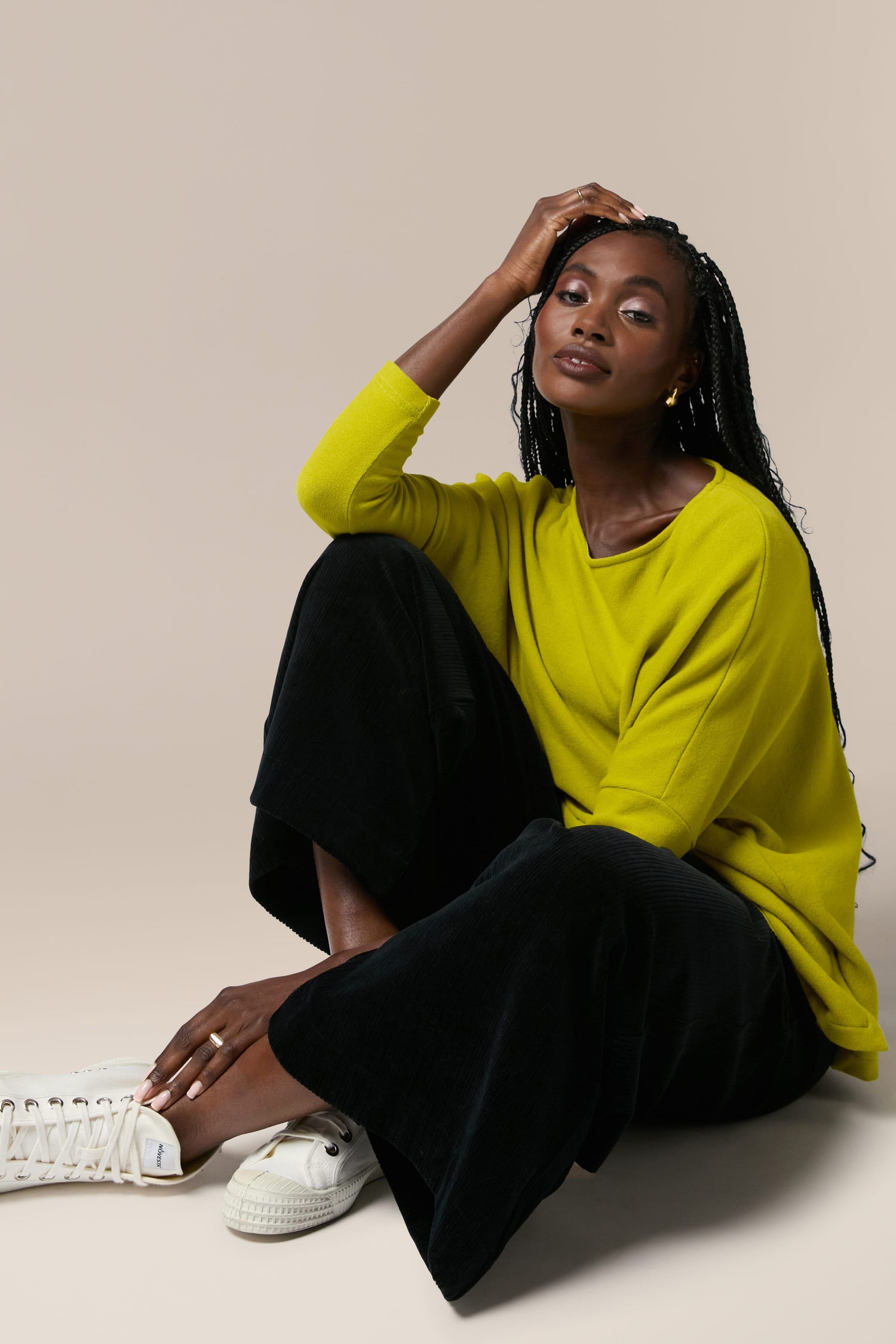 A black woman in a yellow sweater, Mama B, sitting on the floor wearing Bulbo Velvet Wide Leg Trouser made with cord fabric.