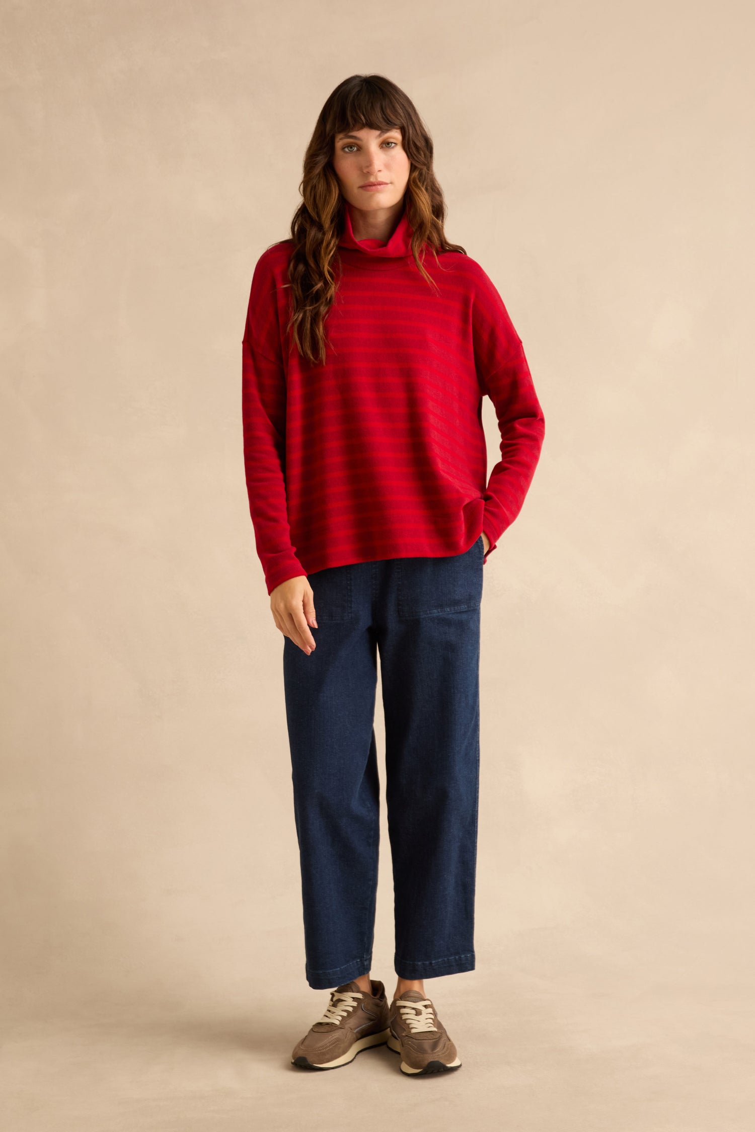 A person wearing a Roll Neck Ruby Wide Stripe Jersey Top and dark blue wide-leg trousers, standing in sneakers.