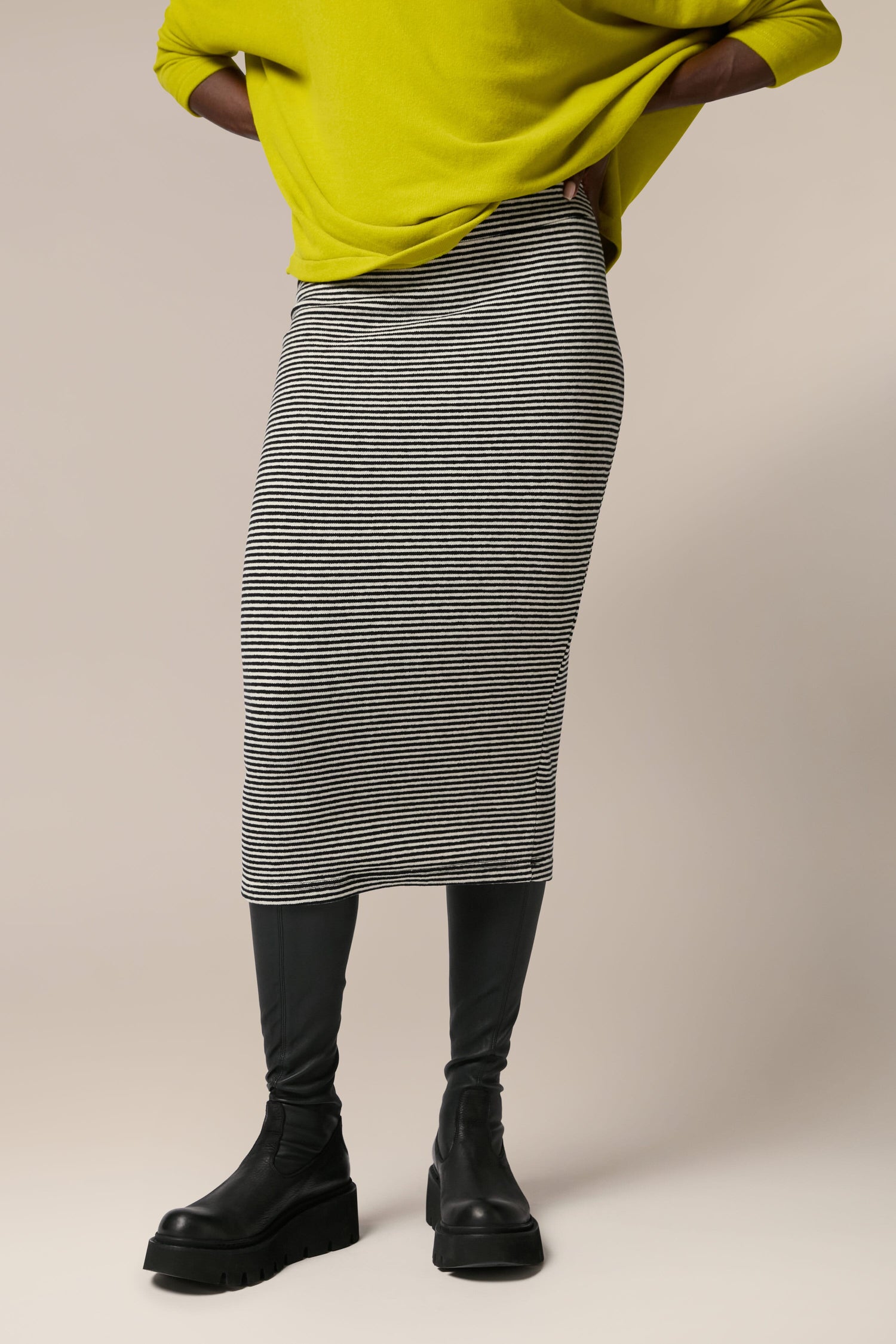 A woman wearing a yellow sweater and grey Lilla Skirt, crafted from soft touch woven fabric, making it an all-occasion garment.