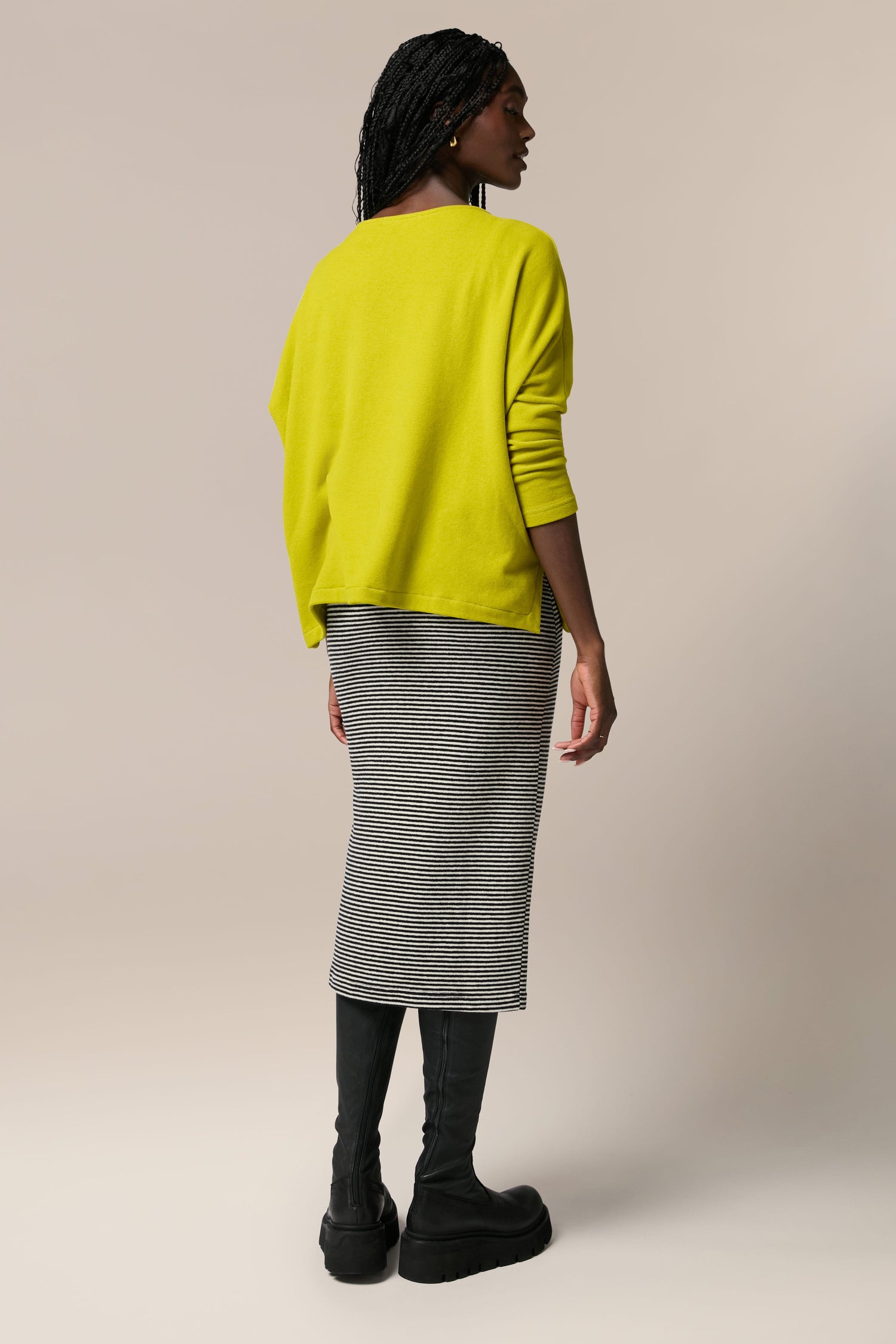 The back view of a woman wearing a yellow sweater and Lilla Skirt, an all-occasion garment made from soft touch woven fabric.