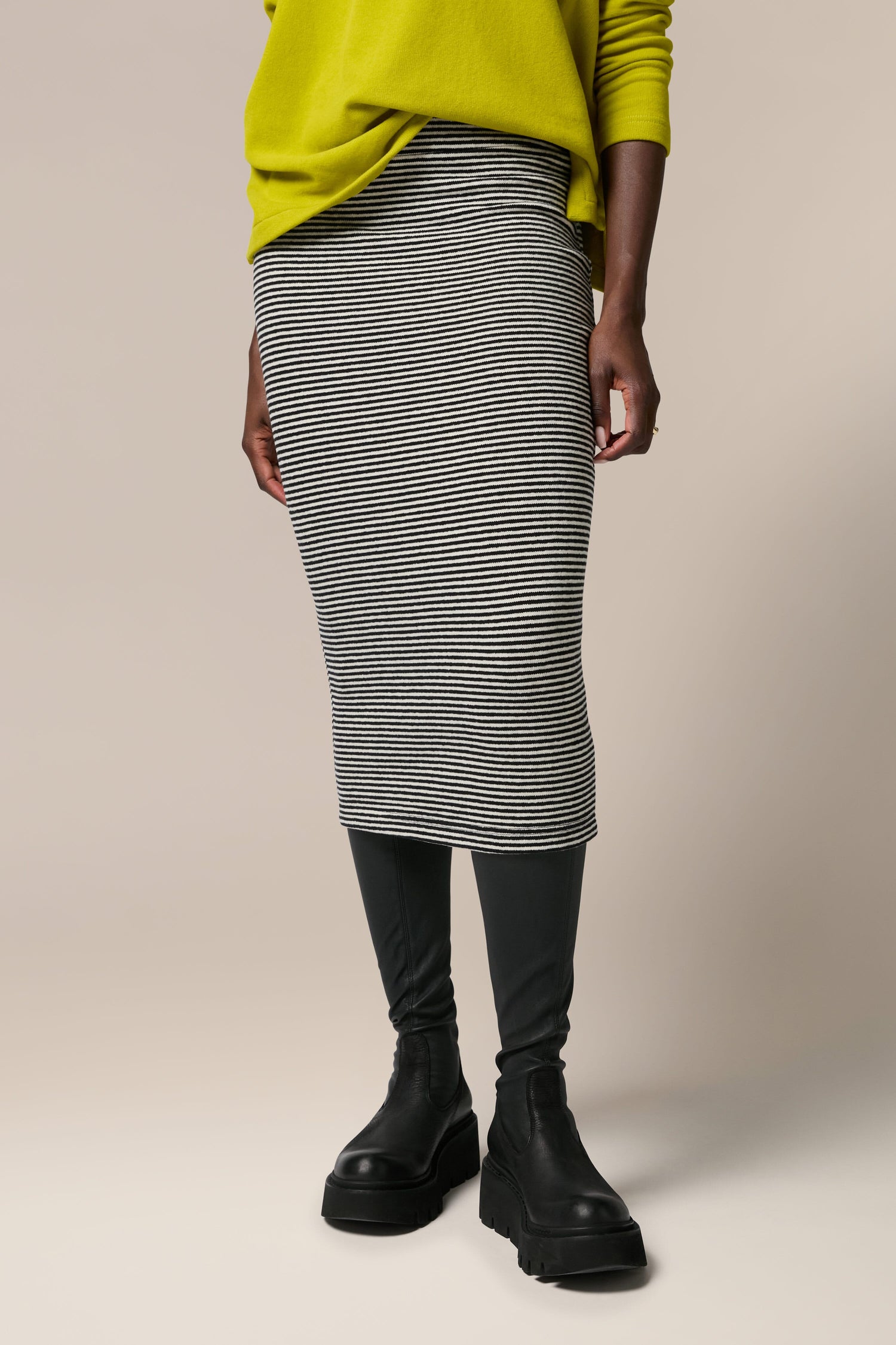 A woman in a yellow sweater and grey Lilla Skirt, made of soft touch woven fabric, perfect for any all-occasion garment.