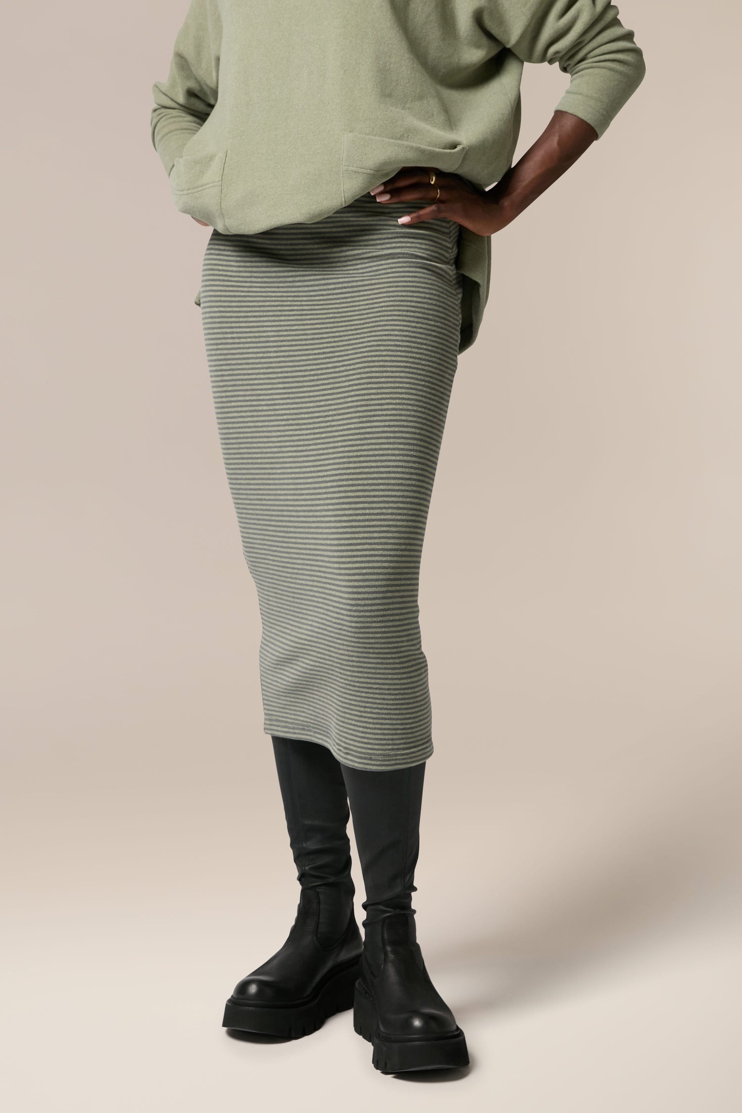 The model is wearing a soft touch woven fabric green sweater and Lilla Skirt.