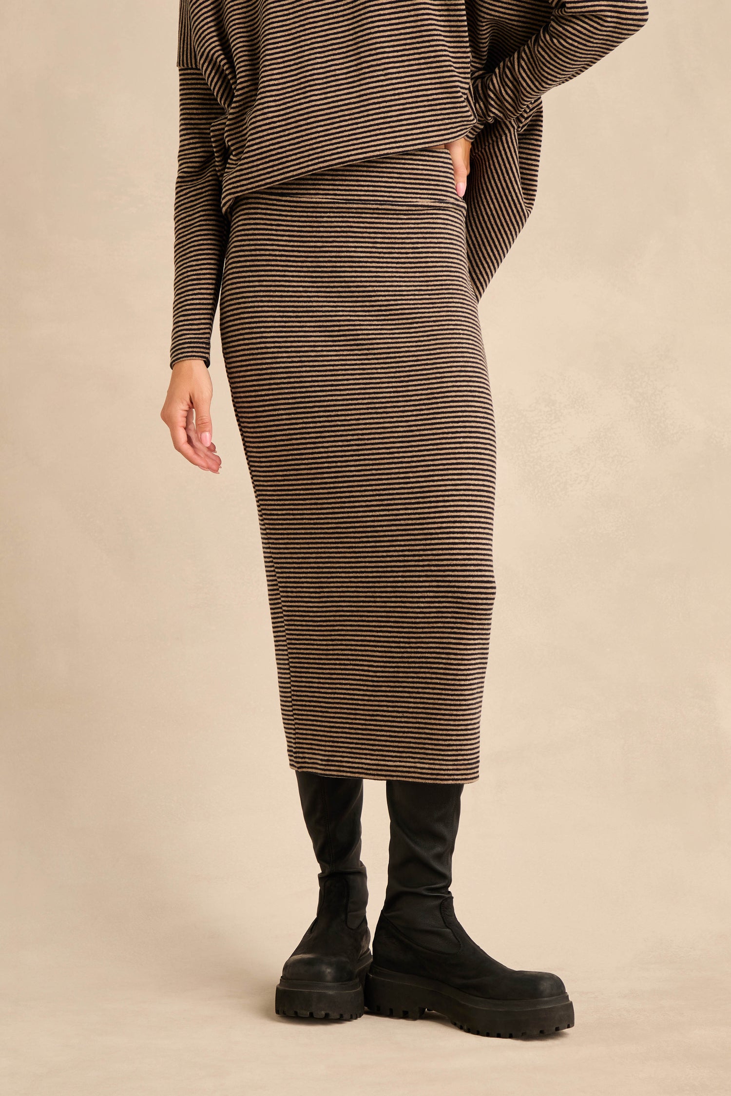A person wearing the Narrow Stripe Jersey Tube Skirt with a matching top and black chunky boots, standing against a plain beige background.