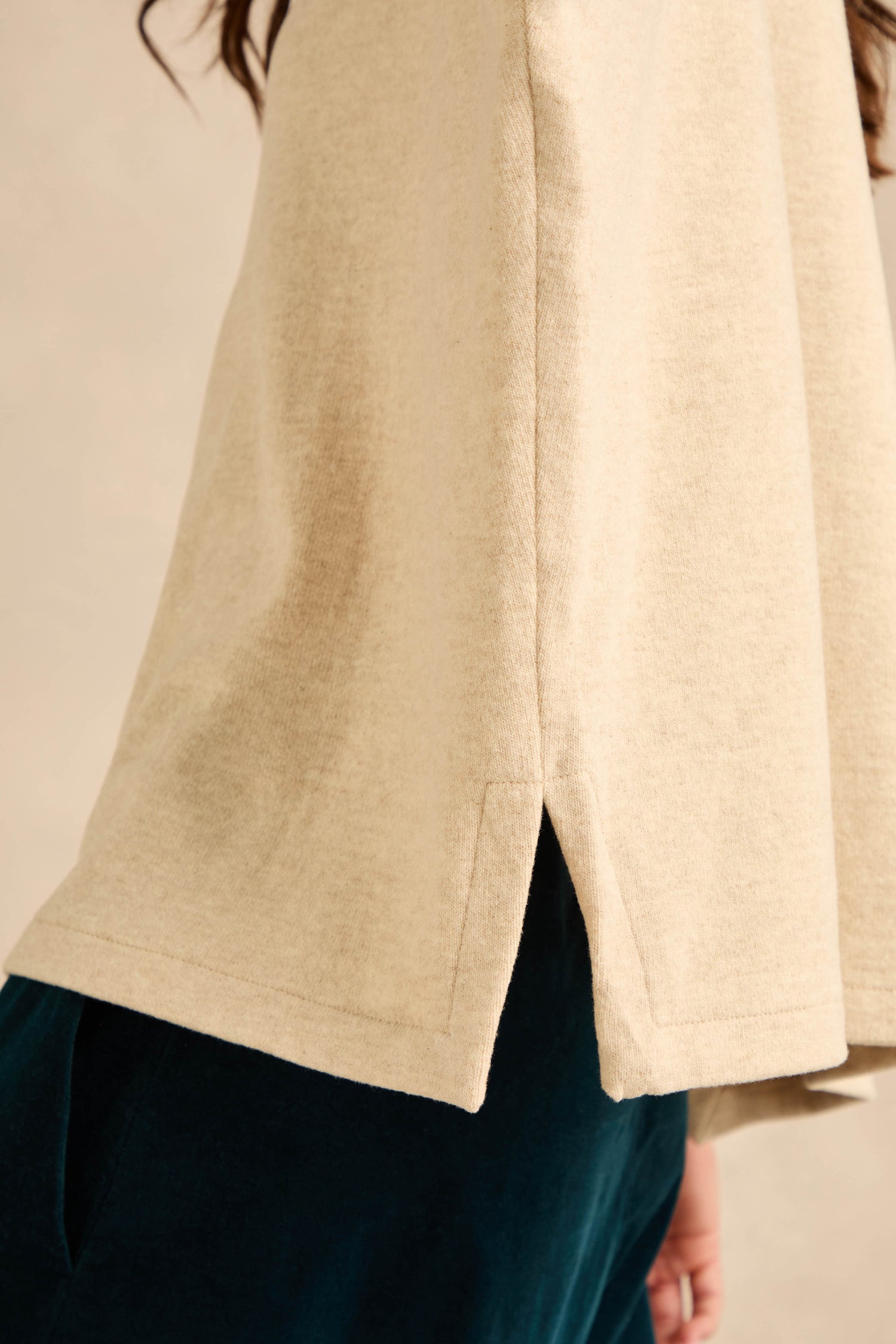Close-up of a person wearing the Round Neck Soft Jersey Top in beige cotton-blend jersey, featuring long sleeves and a side slit hem, paired with dark pants. Shown from shoulder to hip, this top’s relaxed everyday shape and soft fabric add effortless comfort to any look.