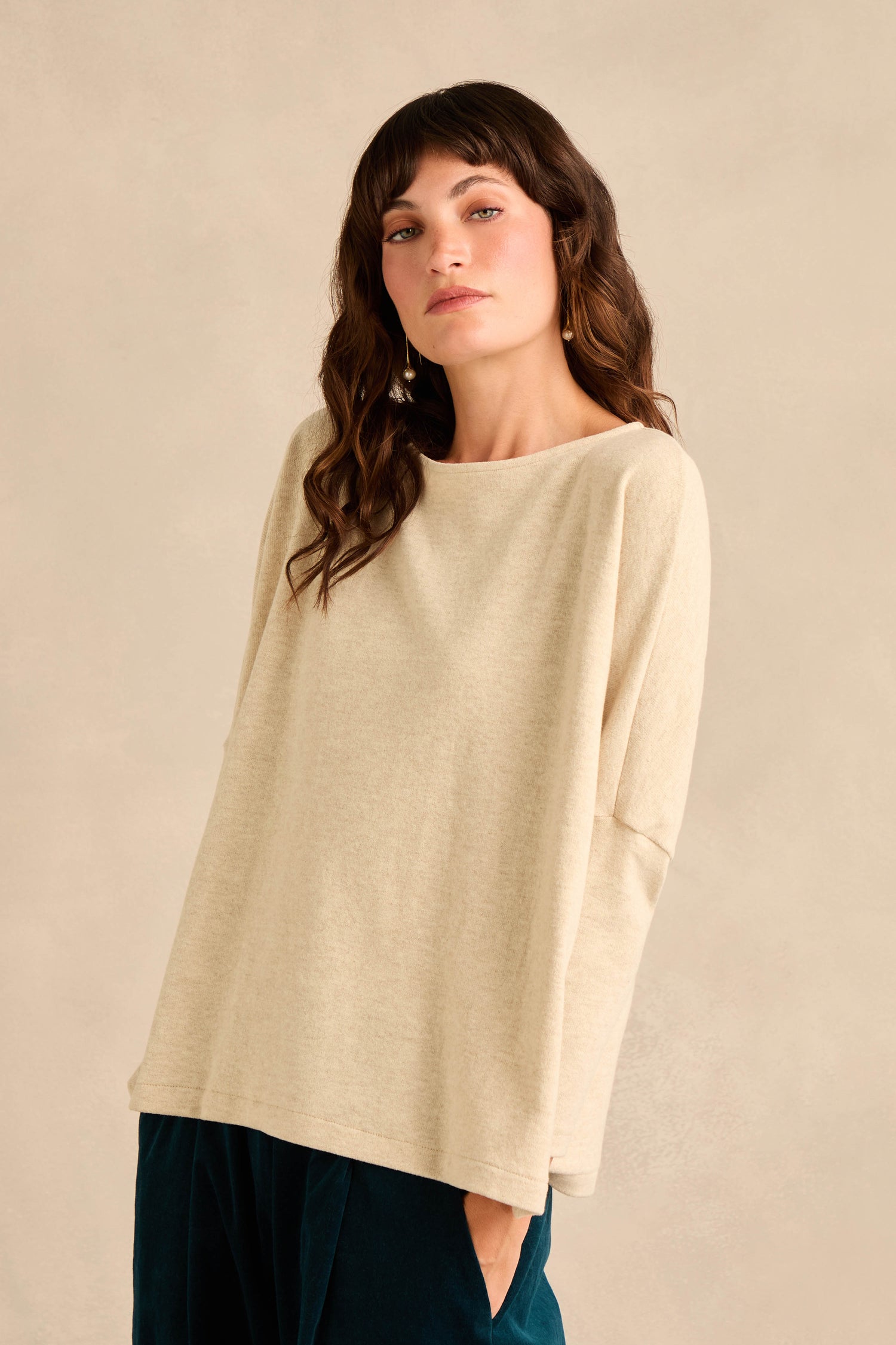 A woman with long brown hair is wearing the Round Neck Soft Jersey Top in a loose, beige cotton-blend style paired with dark pants, standing against a neutral background.