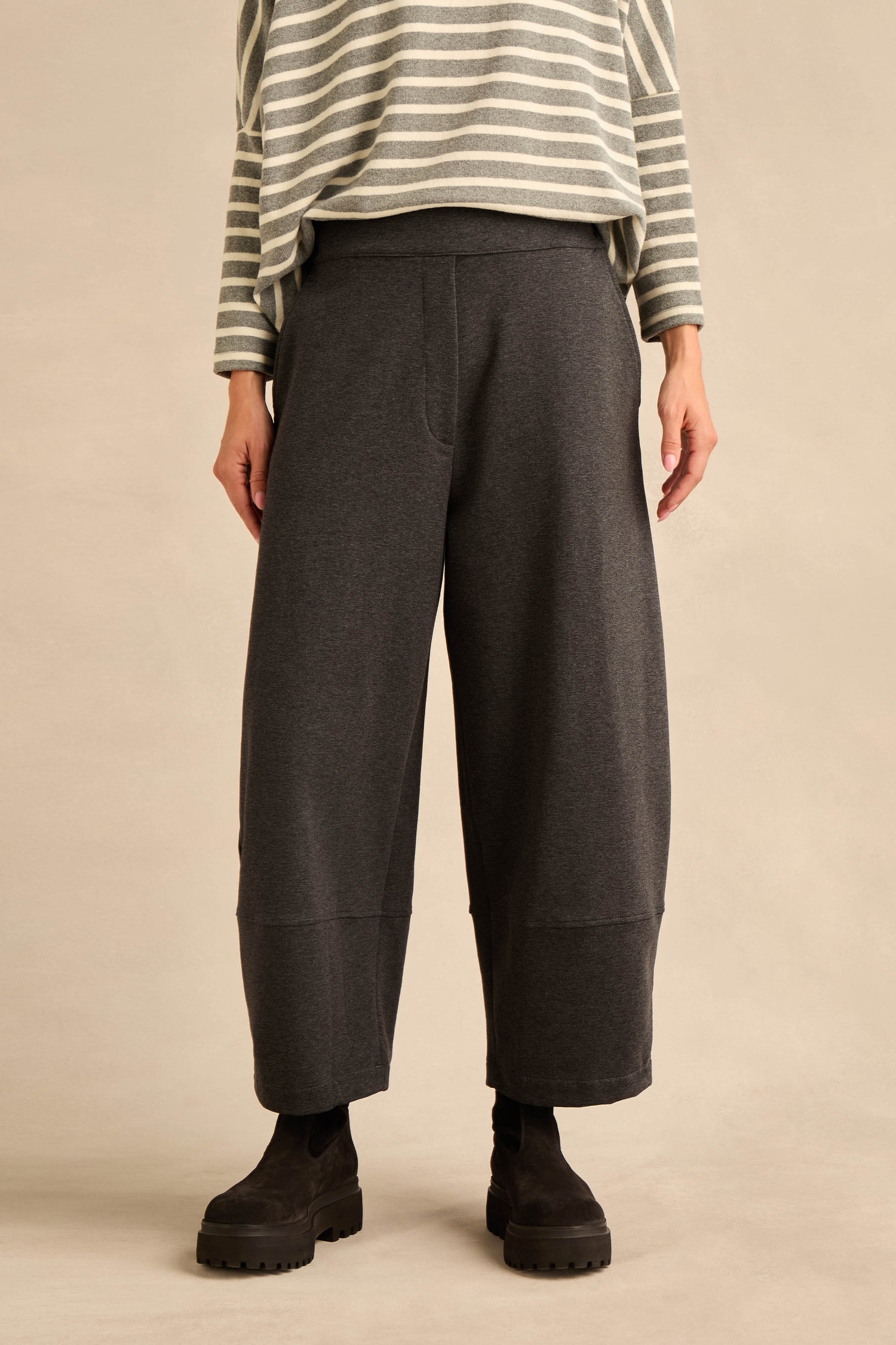 A person stands against a neutral background wearing black boots and the Jersey Pocket Trousers—a wide-leg, dark gray relaxed style—paired with a gray and white striped long-sleeve top crafted from soft cotton stretch jersey.