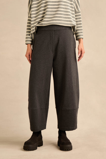 A person stands against a neutral background wearing black boots and the Jersey Pocket Trousers—a wide-leg, dark gray relaxed style—paired with a gray and white striped long-sleeve top crafted from soft cotton stretch jersey.