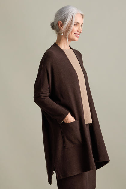 A woman with gray hair is wearing a Souffle Soft Jersey Cardi in a longline length over a beige top, standing against a neutral background. She smiles slightly with her left hand in her cardigan pocket.