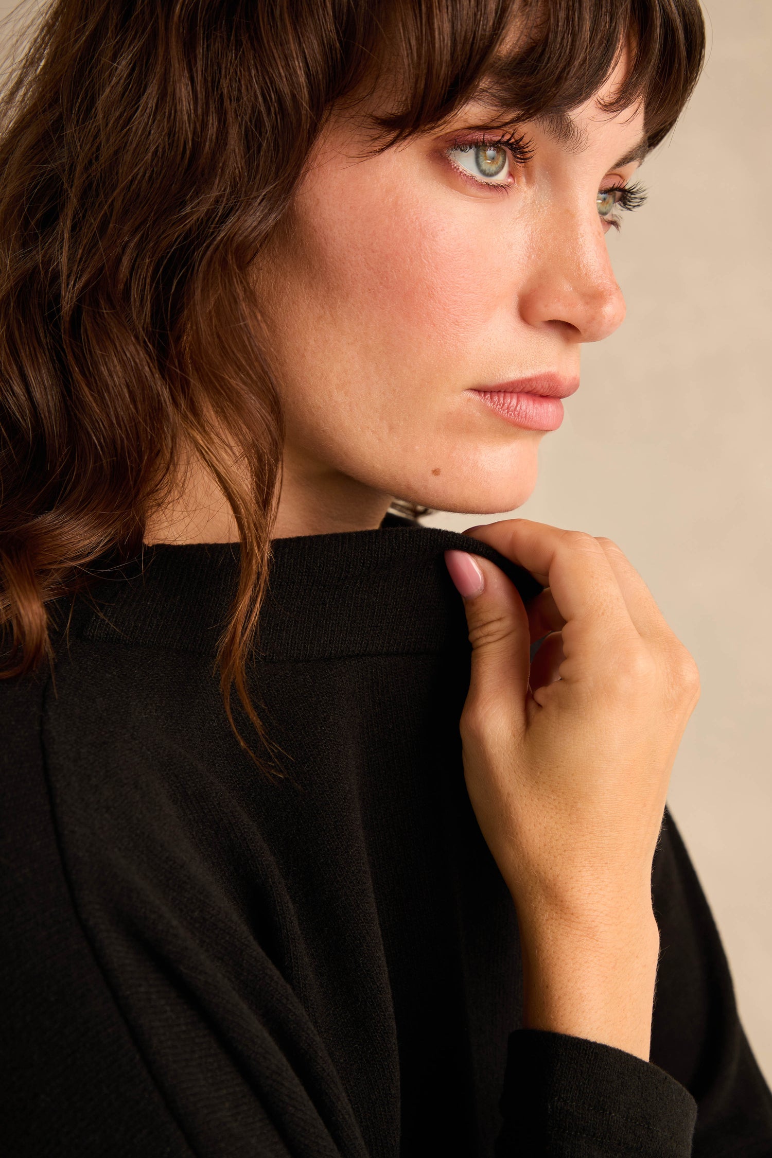 A woman with wavy brown hair and green eyes wears the Black Soft Jersey Boxy Top, looking to the side while holding her collar with her right hand.