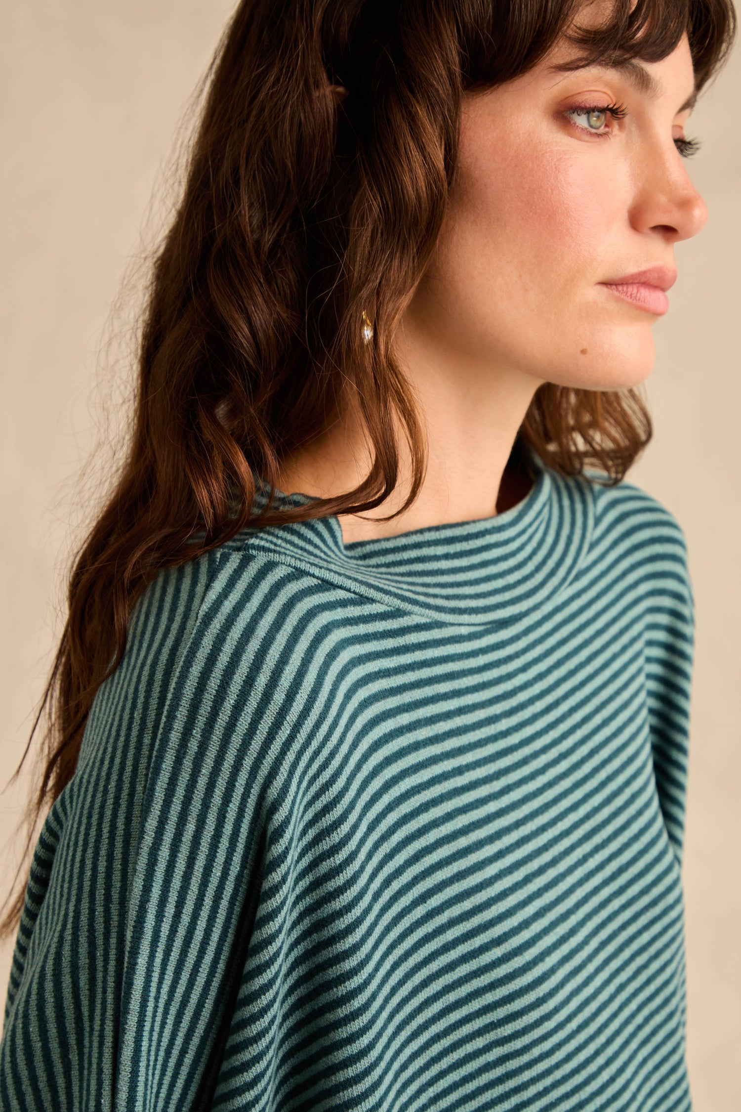 A woman with wavy brown hair wears the Narrow Stripe Soft Jersey Boxy Top in teal and black, looking to the right against a plain light background.