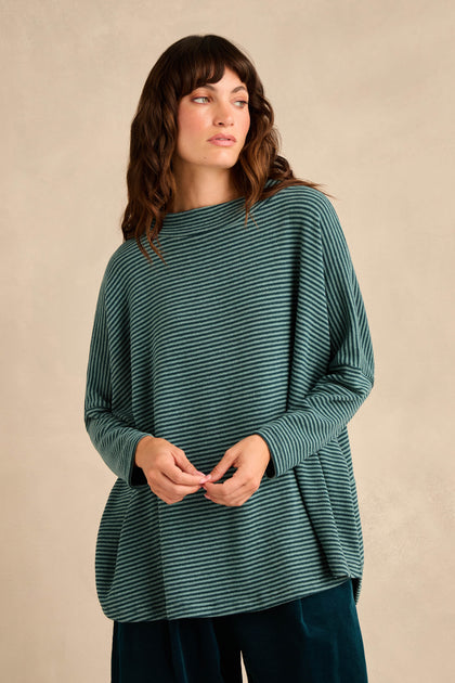 A woman wearing the Narrow Stripe Soft Jersey Boxy Top in green and black with dark pants, standing against a plain beige background.