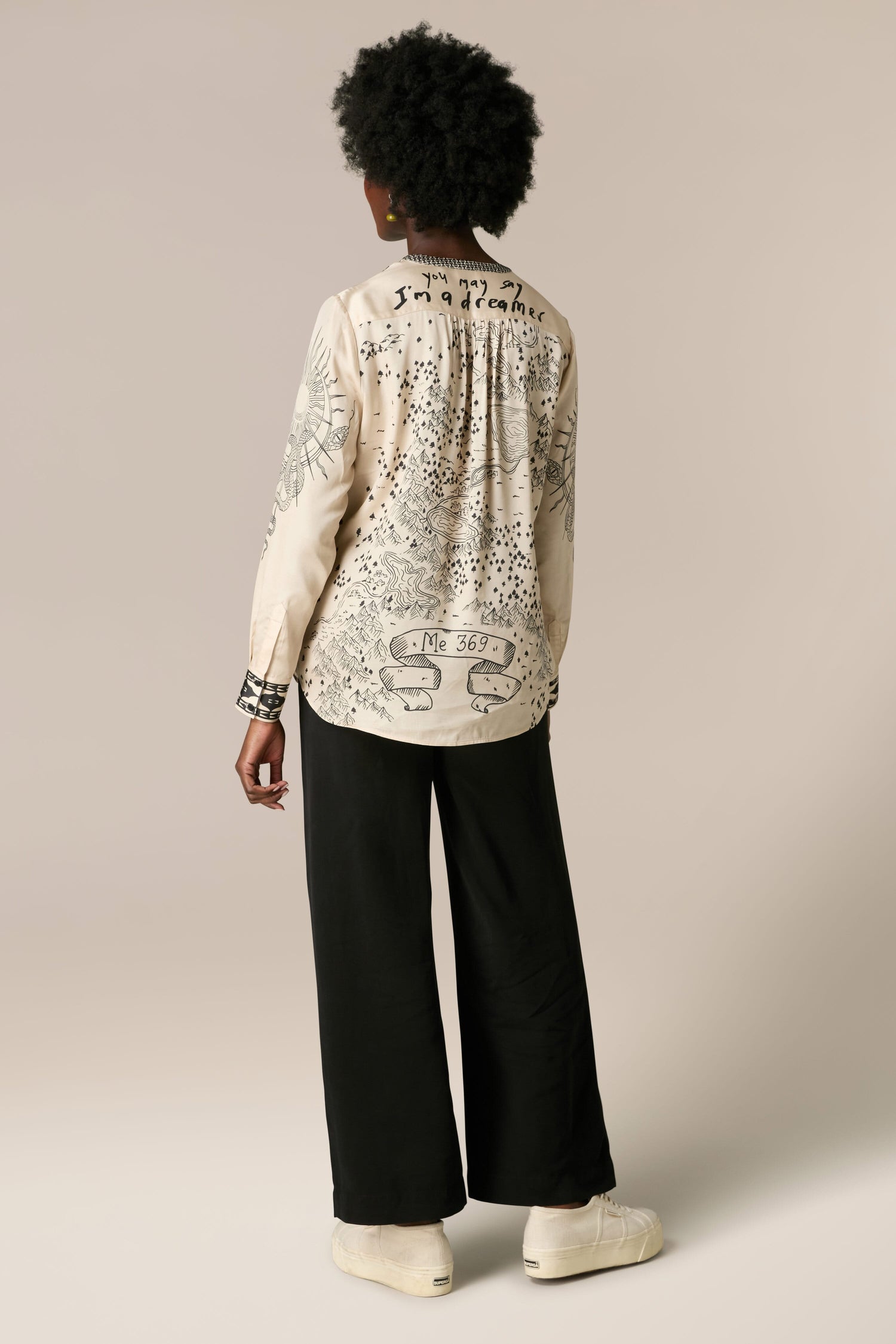 The back view of a woman wearing a Gabriella Bib Front Shirt and black wide leg pants.