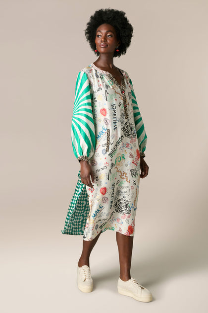 A black woman wearing the Hannah Deep V Neck Graffiti Dress, a green and white printed dress made of silky flowing fabric.