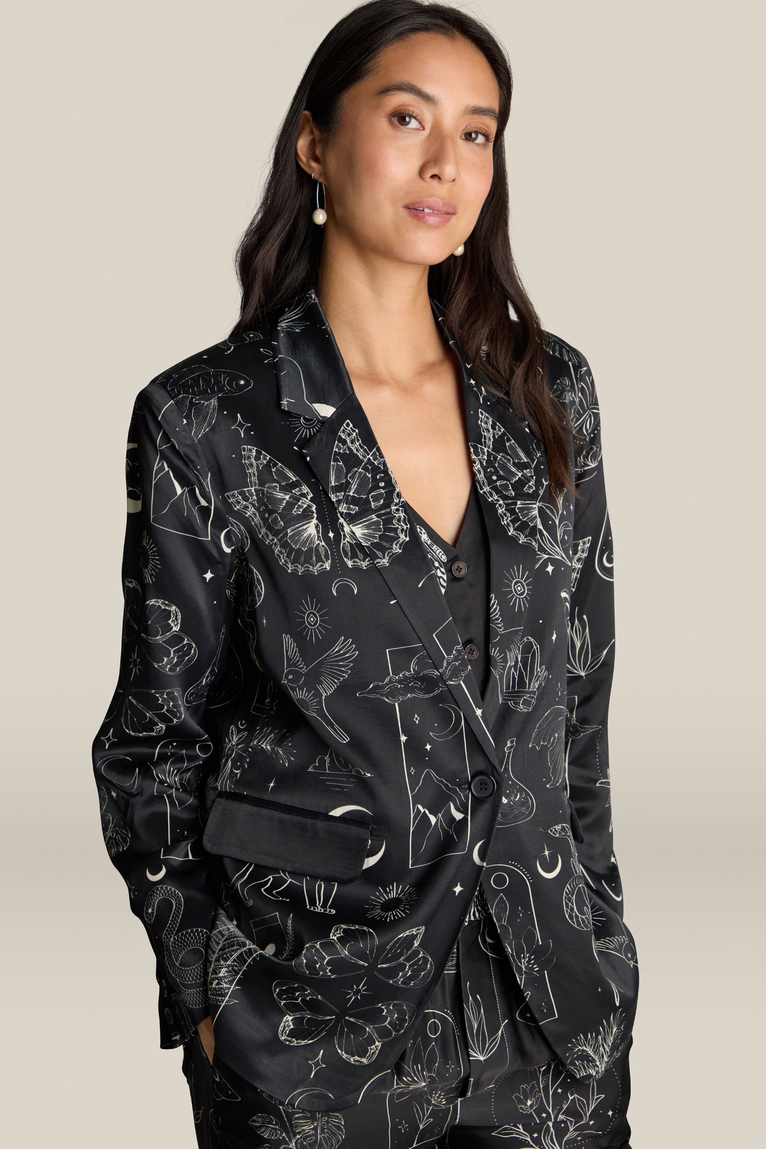 A person with long dark hair stands against a neutral background, wearing the Molly Printed Jacket featuring various white line drawings, elegantly highlighting its luxurious viscose and rayon fabric.