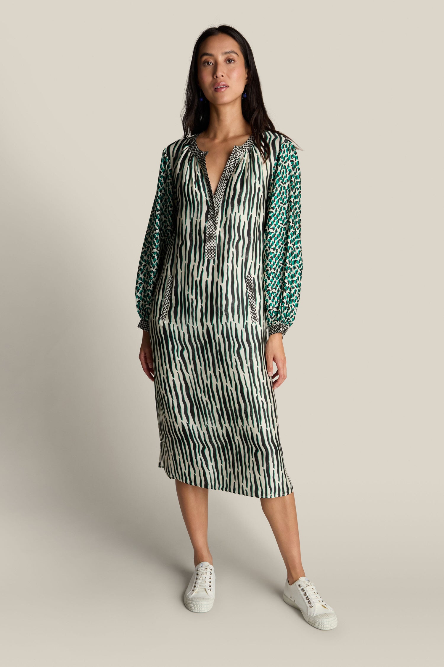 A woman stands wearing the Tropical Hanna Placket Dress and white sneakers against a plain background.