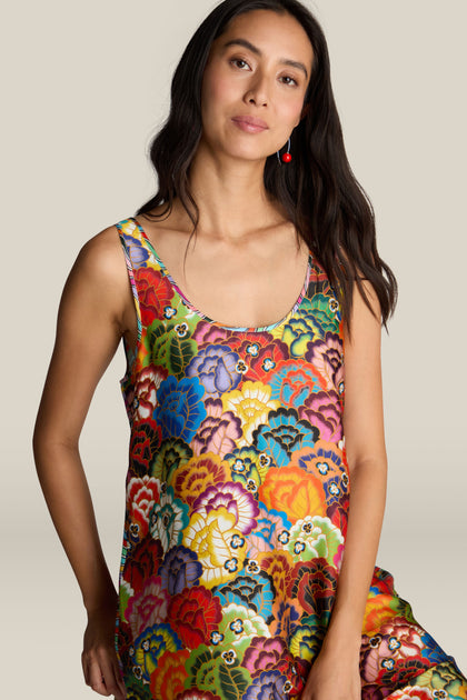 A woman in the Allison Dress, featuring a vibrant floral design and sleeveless cut, stands against a plain background with a slight smile.