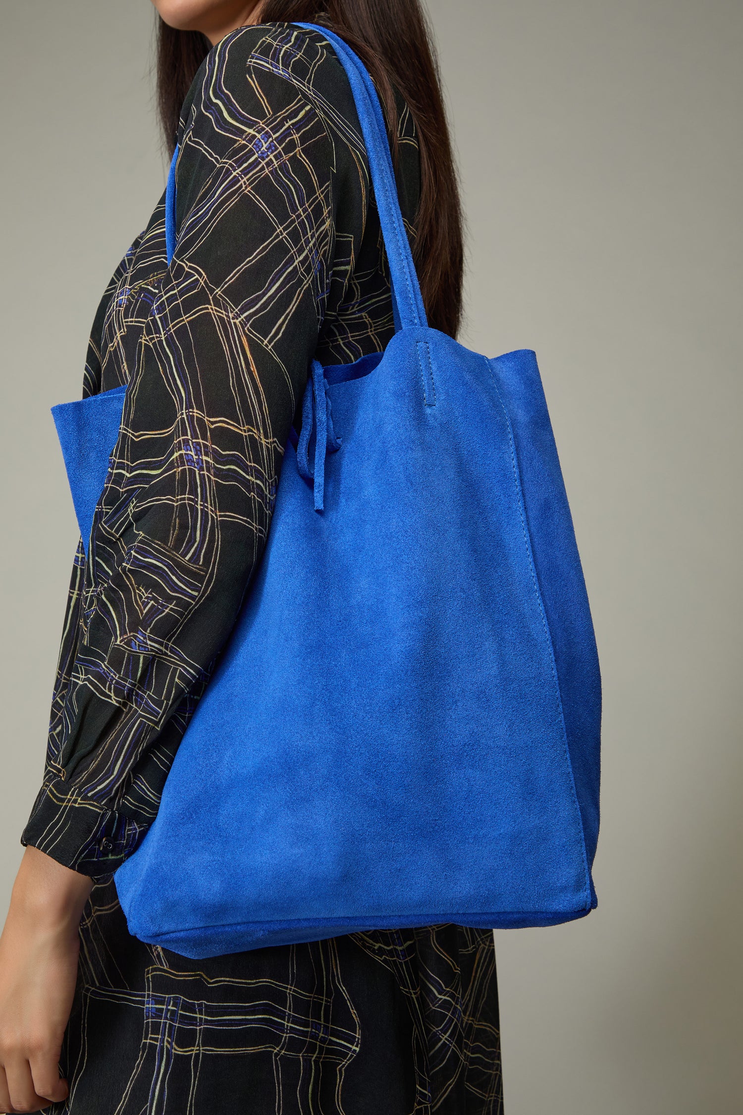 A person carries the Soft Suede Tote Bag over their shoulder, pairing it with a patterned black dress against a plain background.