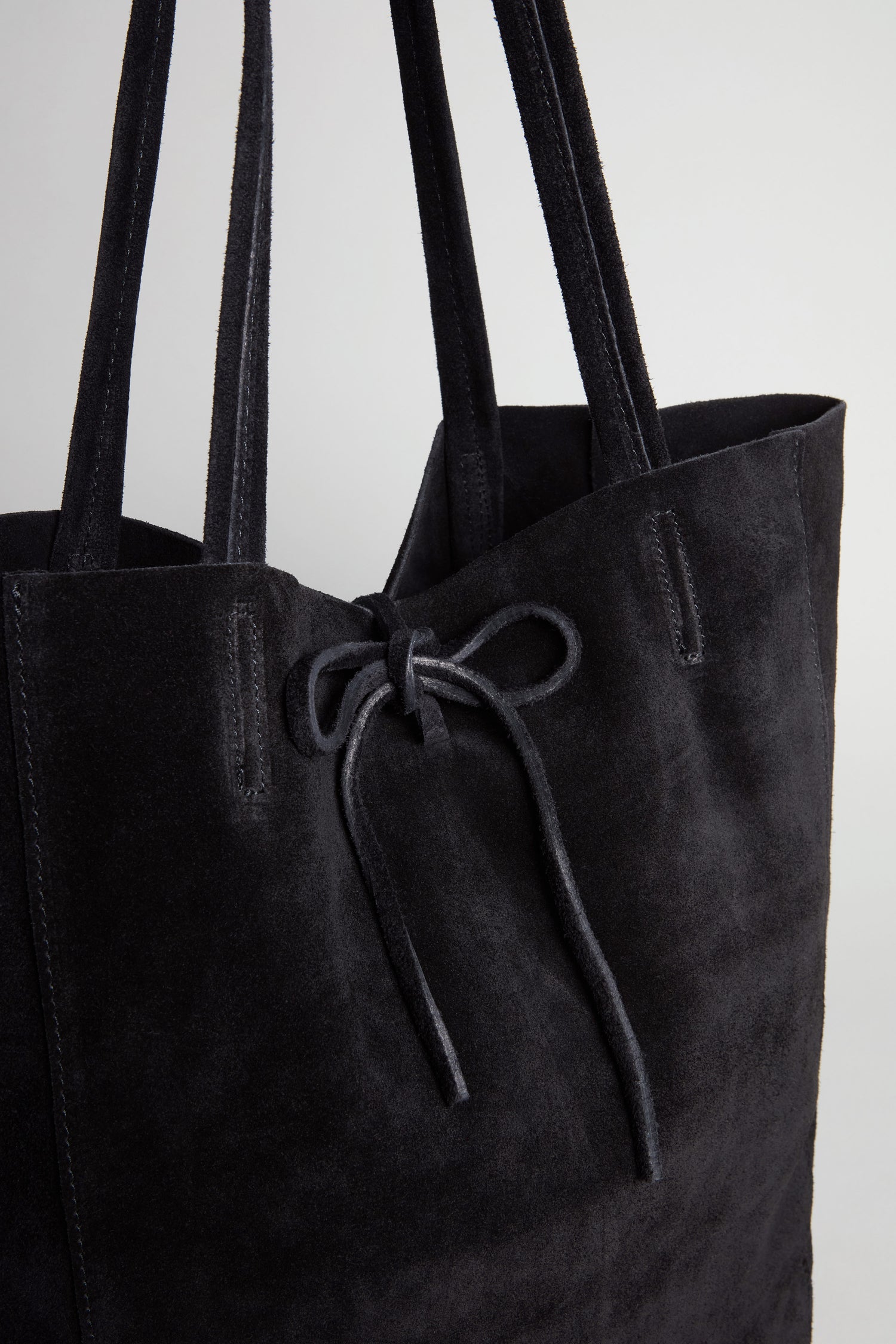 Close-up of the Soft Suede Black Tote Bag, a spacious minimalist tote featuring double handles and a drawstring tie closure, set against a plain light background.