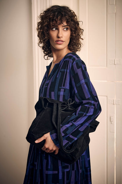 A woman in a blue and black patterned dress holds a spacious, minimalist Black Soft Suede Tote Bag.