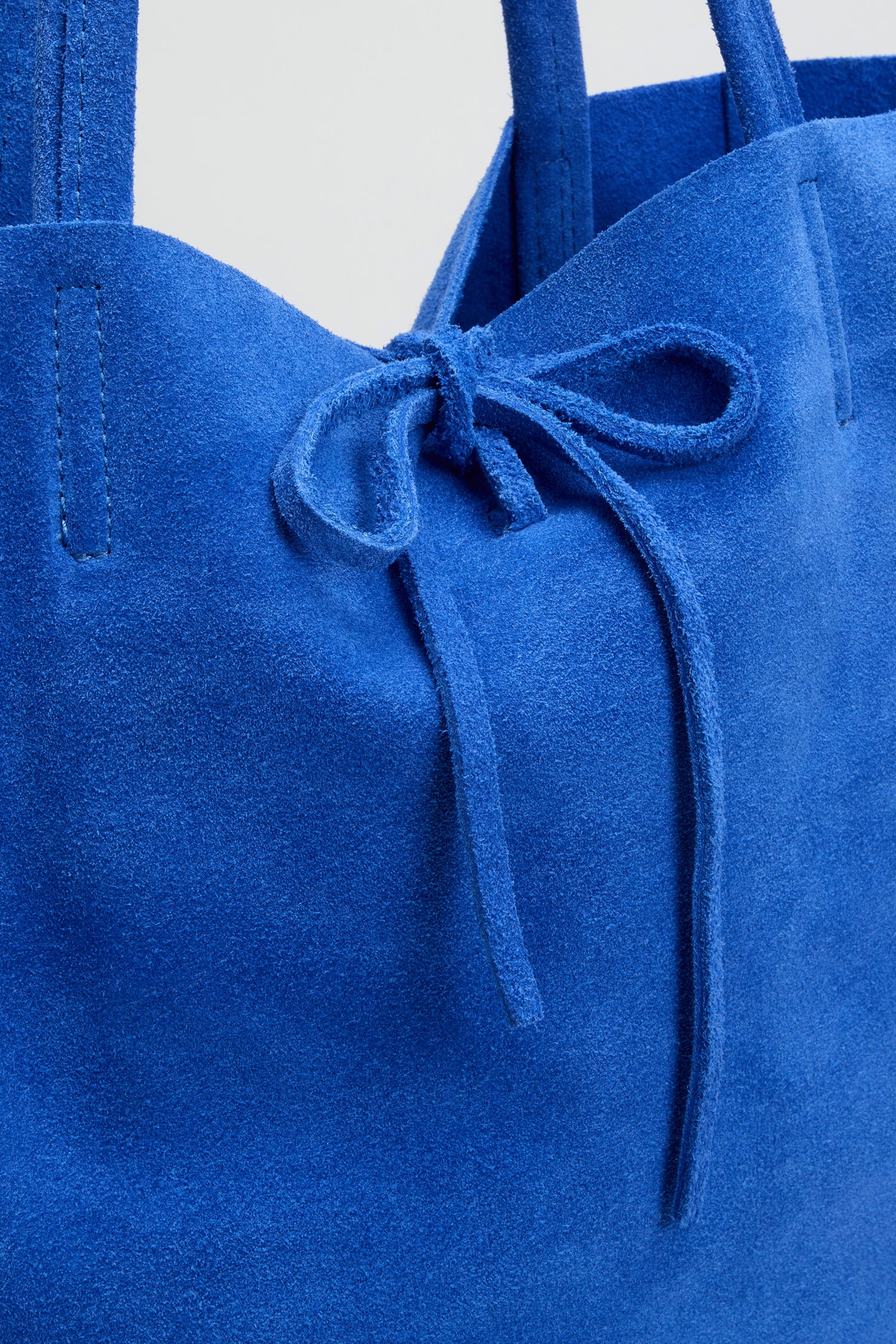 Close-up of the Blue Soft Suede Tote Bag, a luxury piece in bright blue suede, designed with two handles and a bow-tied drawstring closure.