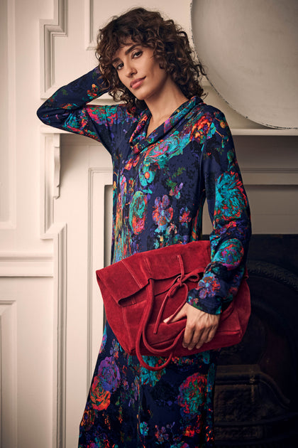 A person in a floral dress holding a large red suede Poppy Soft Suede Tote Bag with a minimalist design.