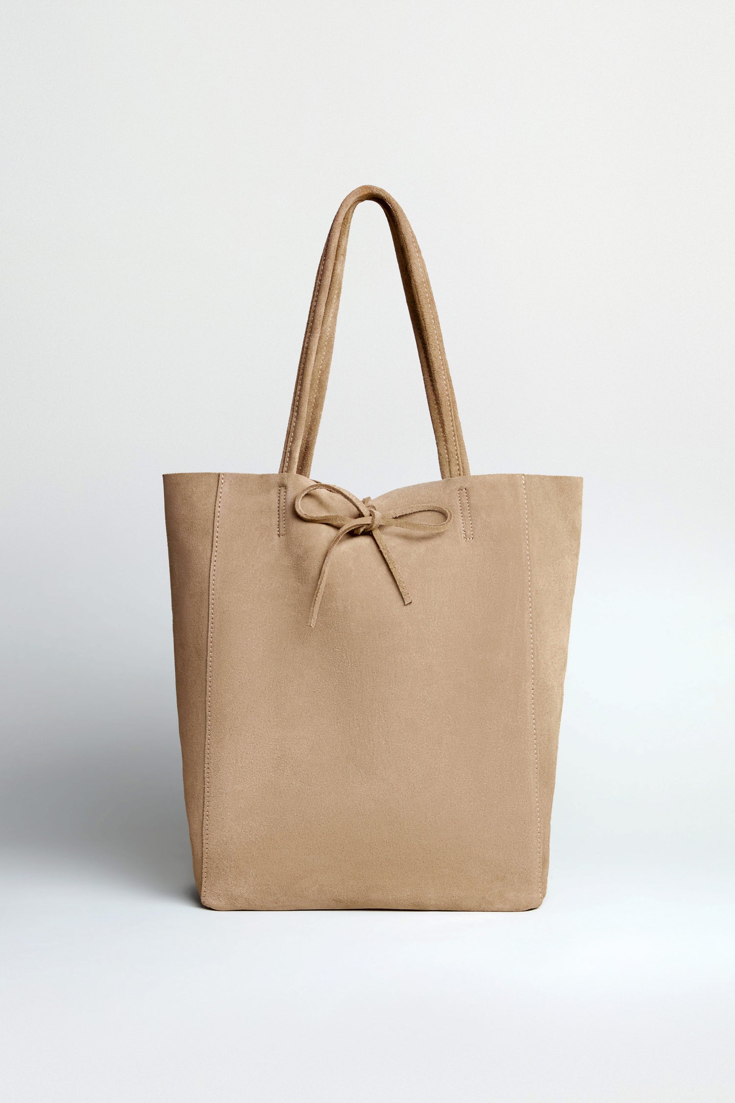 The Soft Suede Sand Tote Bag in beige features a spacious interior, two handles, and a front bow detail, shown against a plain light background.