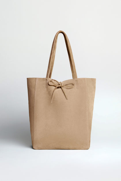 The Soft Suede Sand Tote Bag in beige features a spacious interior, two handles, and a front bow detail, shown against a plain light background.