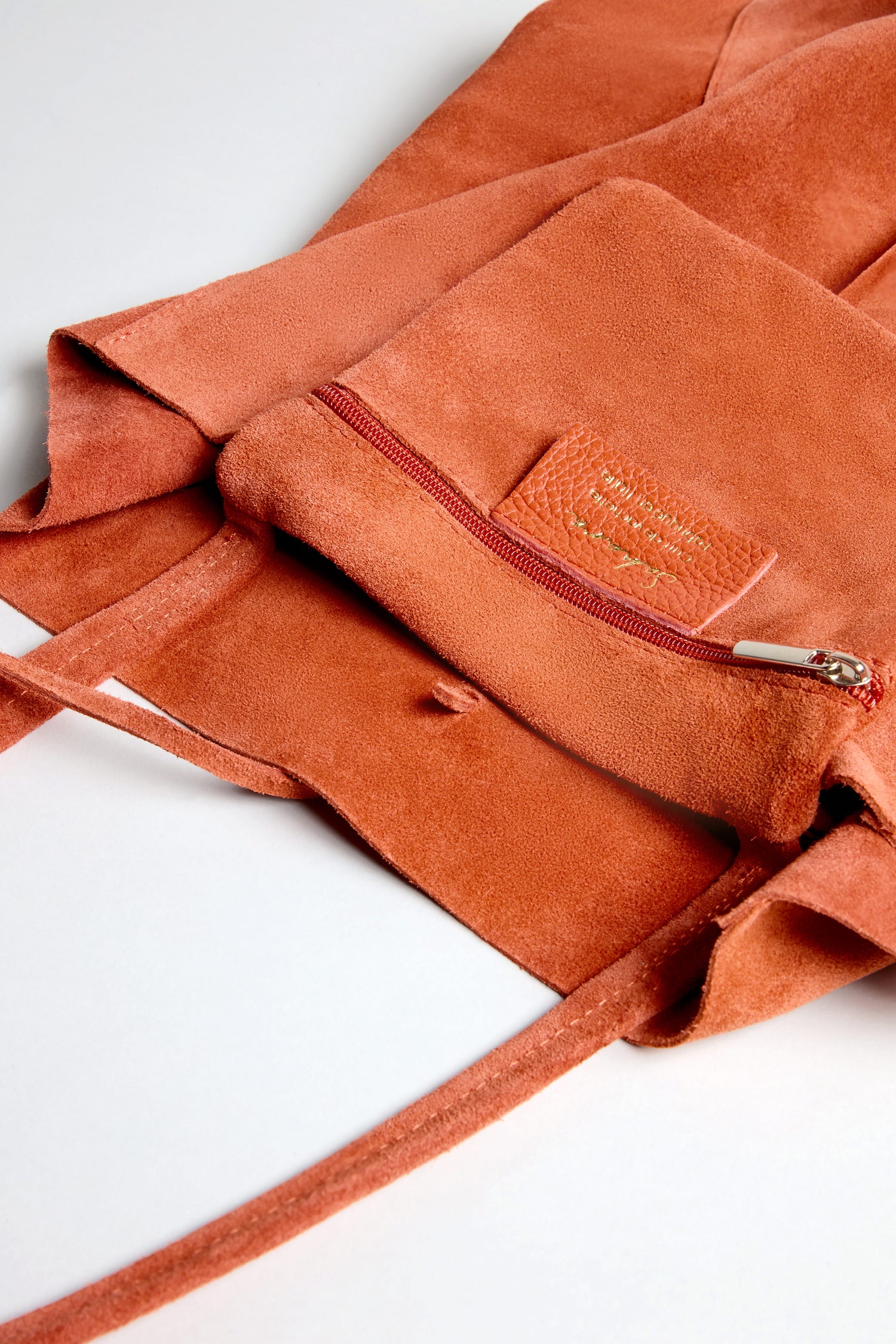 Close-up of the Soft Suede Tangerine Tote Bag open on a white surface, featuring a spacious interior, zippered front pocket, and long strap.