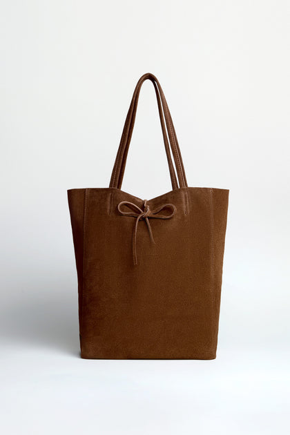 The Soft Suede Chocolate Tote Bag features double handles and a decorative front bow, set against a plain white background—perfect for adding effortless elegance to any outfit.