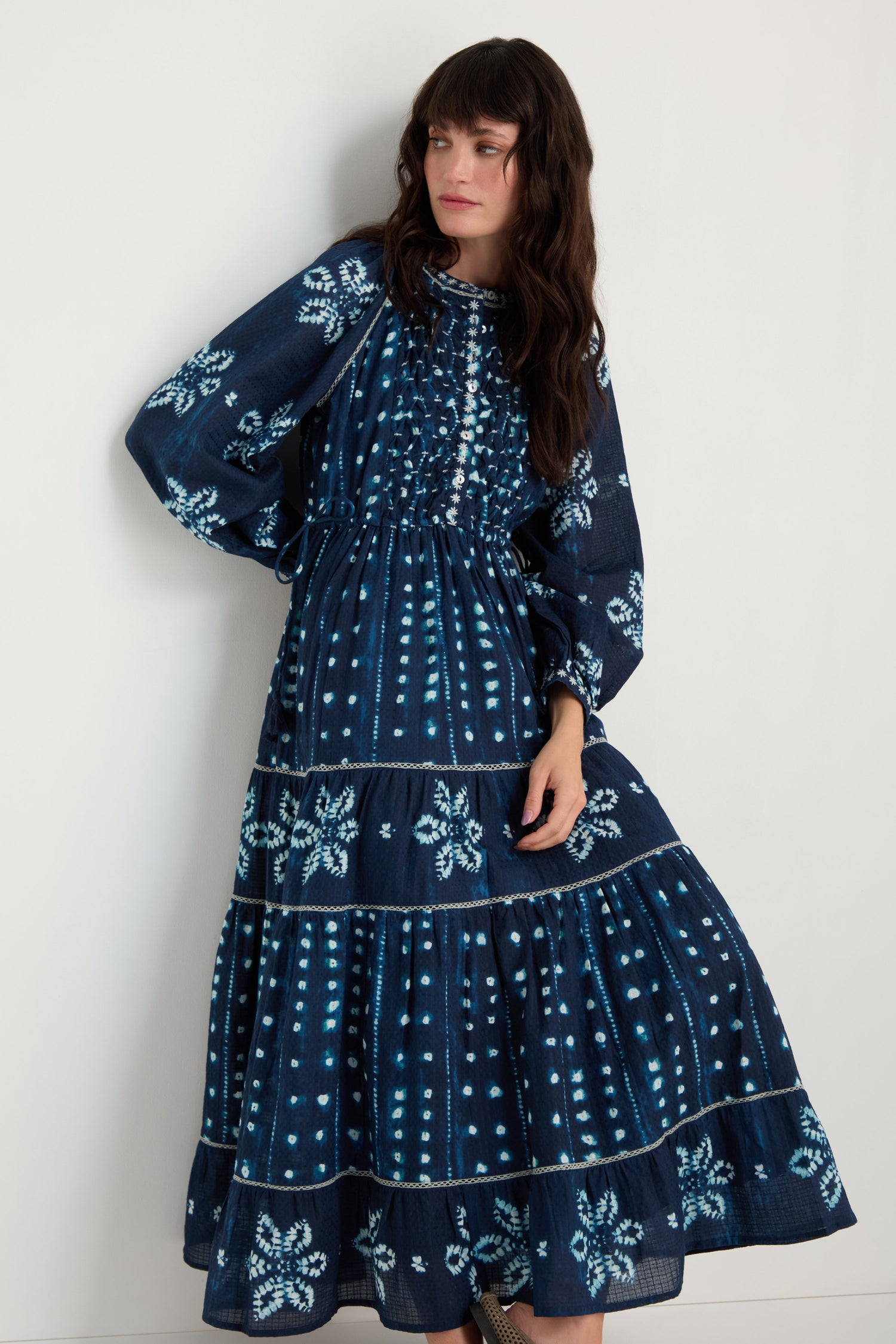 Woman wearing the Mixed Shibori Dress, made of pure cotton in navy blue with white floral and dot patterns, standing against a plain white wall.