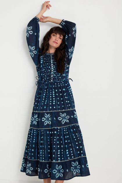 A woman wears the Mixed Shibori Dress, featuring long sleeves and navy blue fabric with light blue floral and dotted patterns, standing against a plain white background.