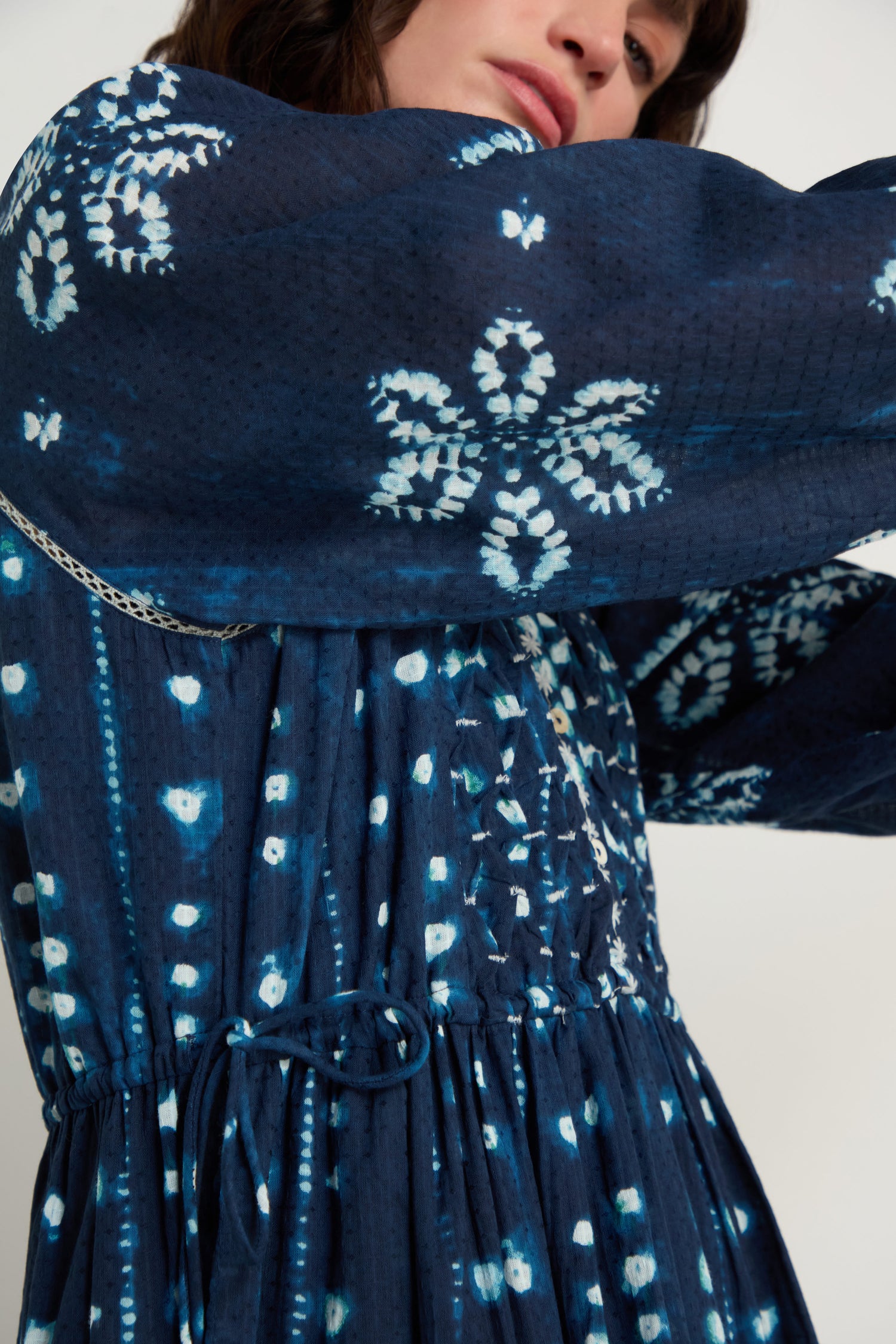 A person wearing the Mixed Shibori Dress—a dark blue midi dress with white tie-dye patterns, long sleeves, a drawstring-gathered waist, and classic styling.