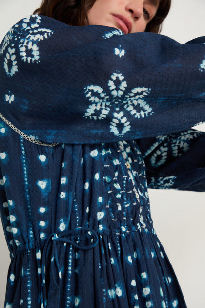 A person wearing the Mixed Shibori Dress—a dark blue midi dress with white tie-dye patterns, long sleeves, a drawstring-gathered waist, and classic styling.