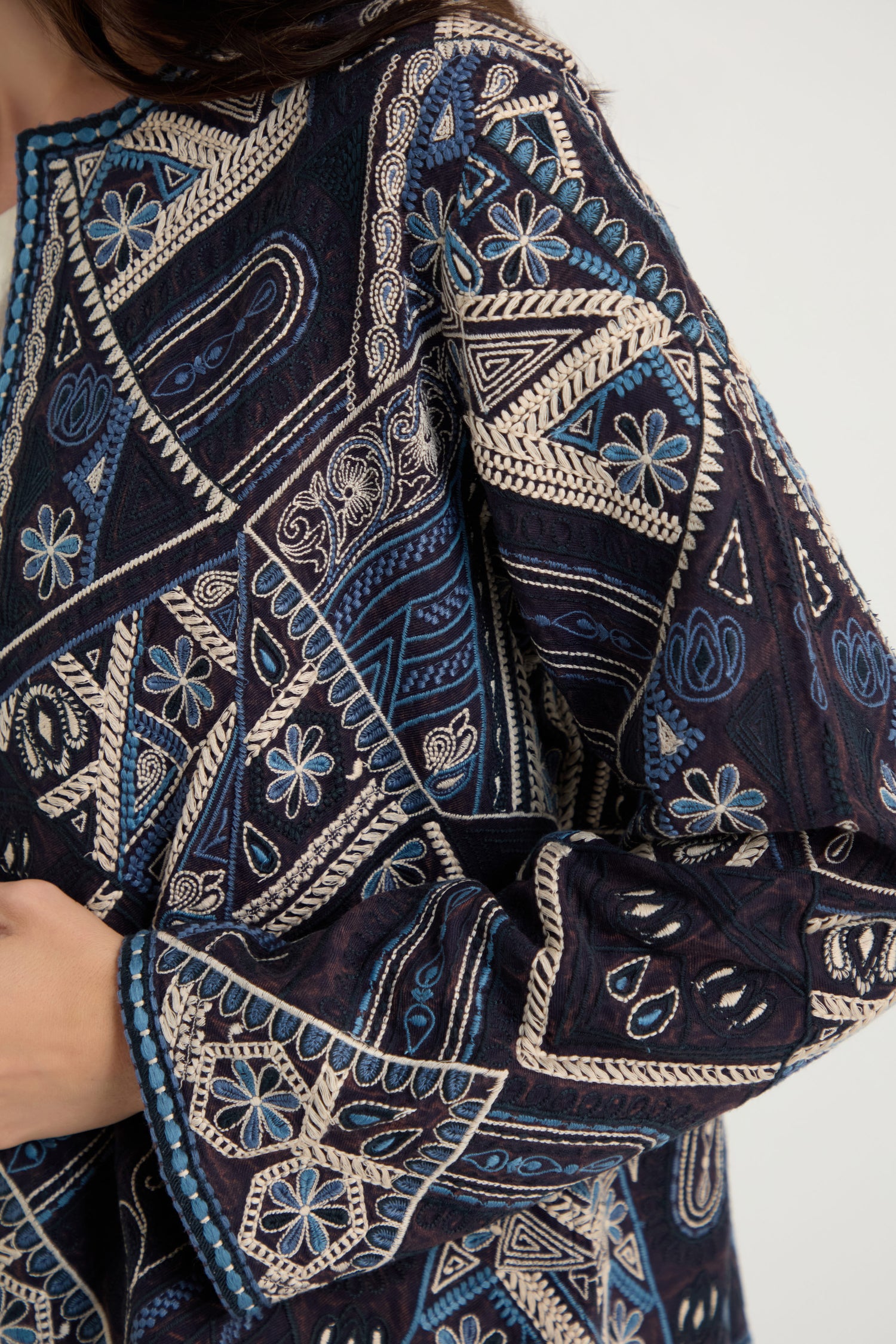 A close-up of a person wearing the Embroidered Mosaic Jacket in dark blue and cream, highlighting its intricate geometric and floral embroidery with a modern boxy silhouette.