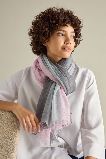 Person wearing a white shirt and the St Tropez Cashmere Shawl, featuring pink and grey tones, handcrafted in Nepal, sitting against a neutral background.