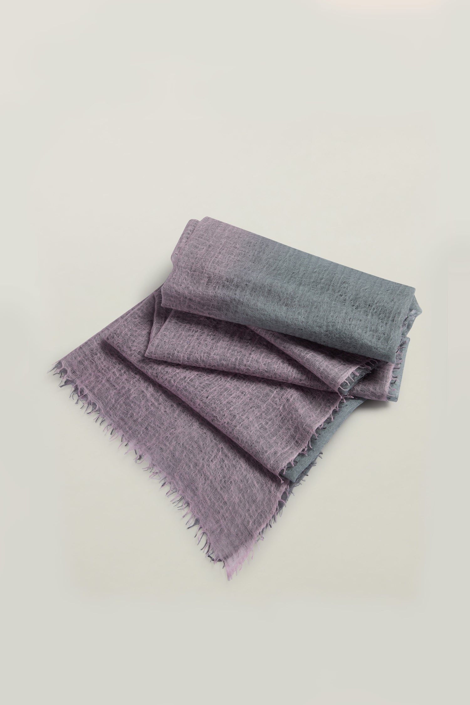 The St Tropez Cashmere Shawl, folded and featuring purple-gray ombre with fringed edges, is handcrafted in Nepal using ethical practices.