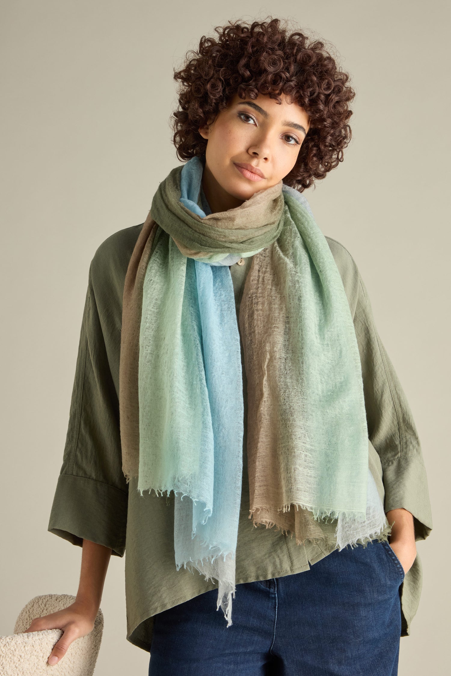 Against a neutral background stands a person with curly hair, wearing a green shirt and the St Tropez Cashmere Shawl—multicolored and handcrafted in Nepal.