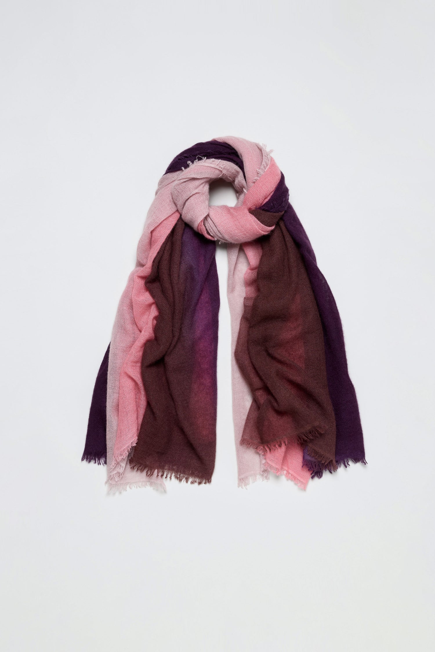 The Cherry and Pink Soft Colourblend Cashmere Shawl, featuring a multicolored ombré blend of pink, mauve, and purple tones, is loosely folded with frayed edges, woven in Nepal, and displayed against a plain white background.