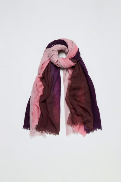 The Cherry and Pink Soft Colourblend Cashmere Shawl, featuring a multicolored ombré blend of pink, mauve, and purple tones, is loosely folded with frayed edges, woven in Nepal, and displayed against a plain white background.