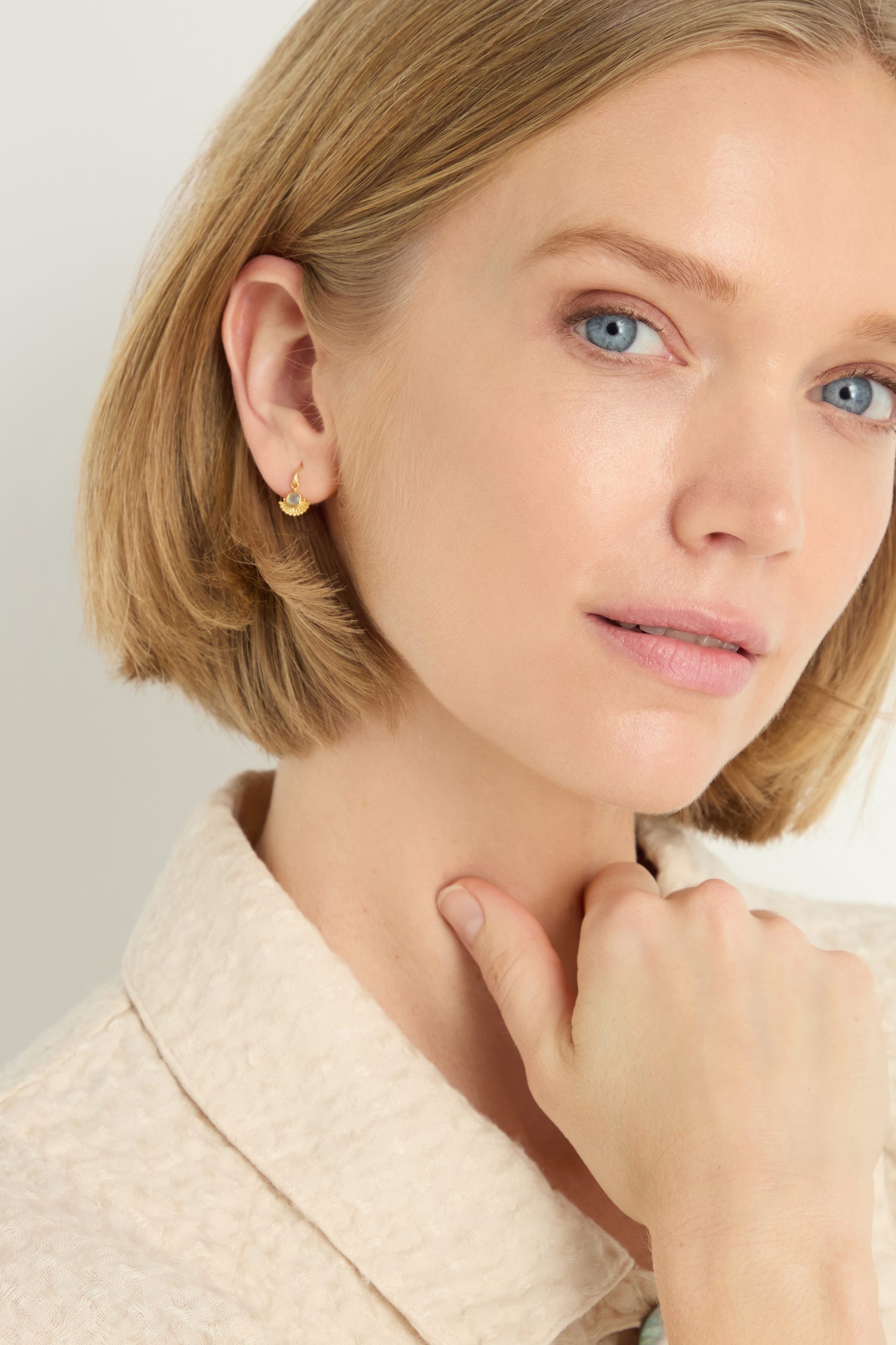 A woman with blonde hair and blue eyes wears Gold Plated Labradorite Sunburst Earrings, adding a radiant touch to her look.