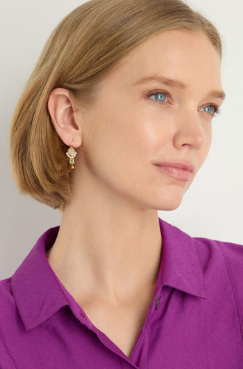 A woman with short blonde hair in a purple collared shirt and Gold Plated White Moonstone Ariel Earrings looks slightly to the side against a light background.