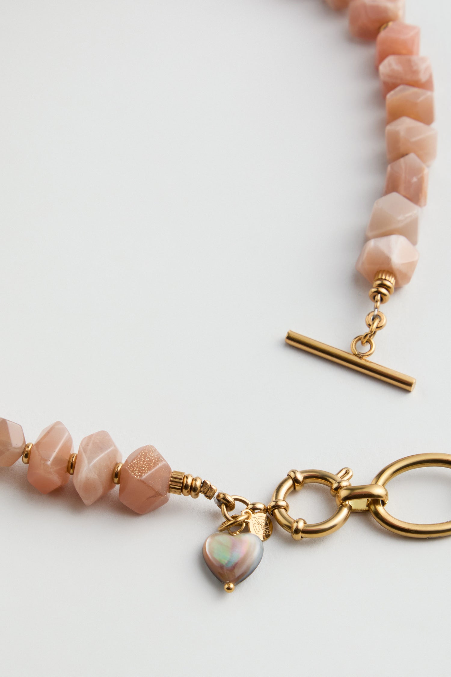 The Amazonite Bead Necklace features faceted pink stones, a gold toggle clasp, a heart-shaped charm near the closure, and subtle amazonite bead accents for a touch of blue-green beauty.